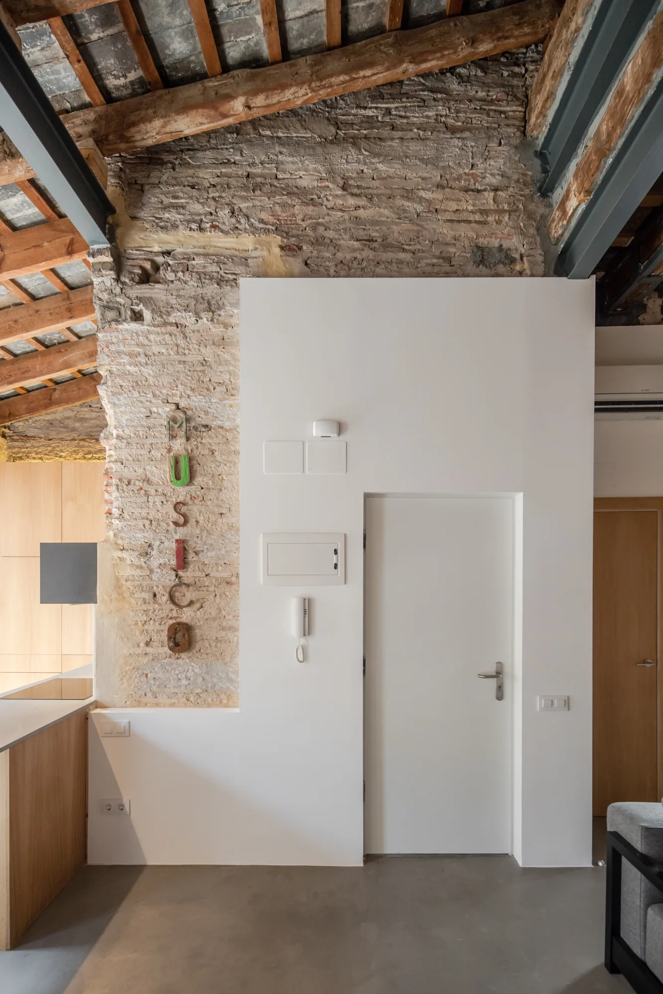 A modern white partition wall with a door stands against a rustic background of exposed brick and timber ceiling beams.