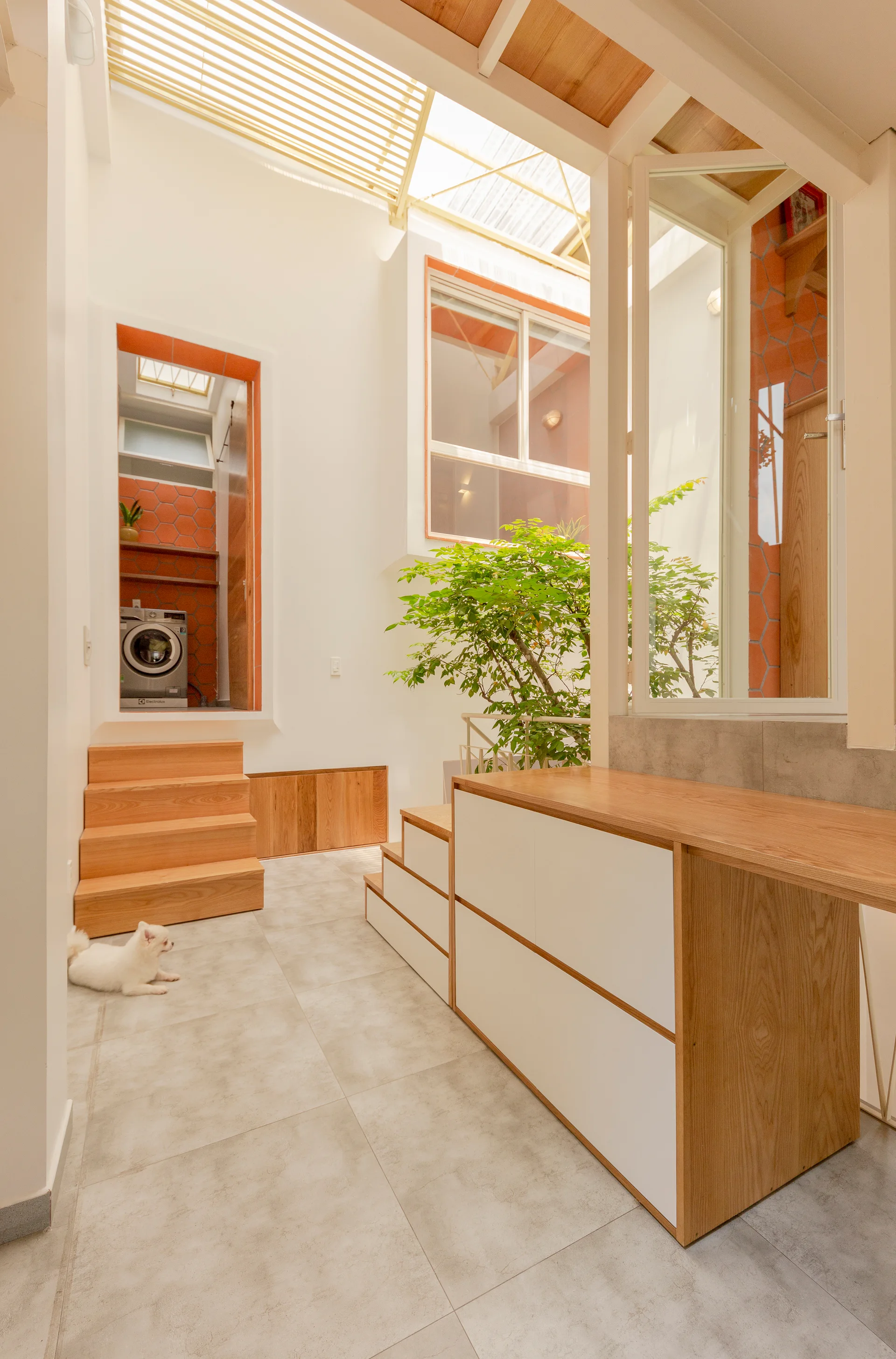 A split-level interior hallway with light wood steps, built-in storage drawers, and a view of a raised laundry room under a slatted skylight.