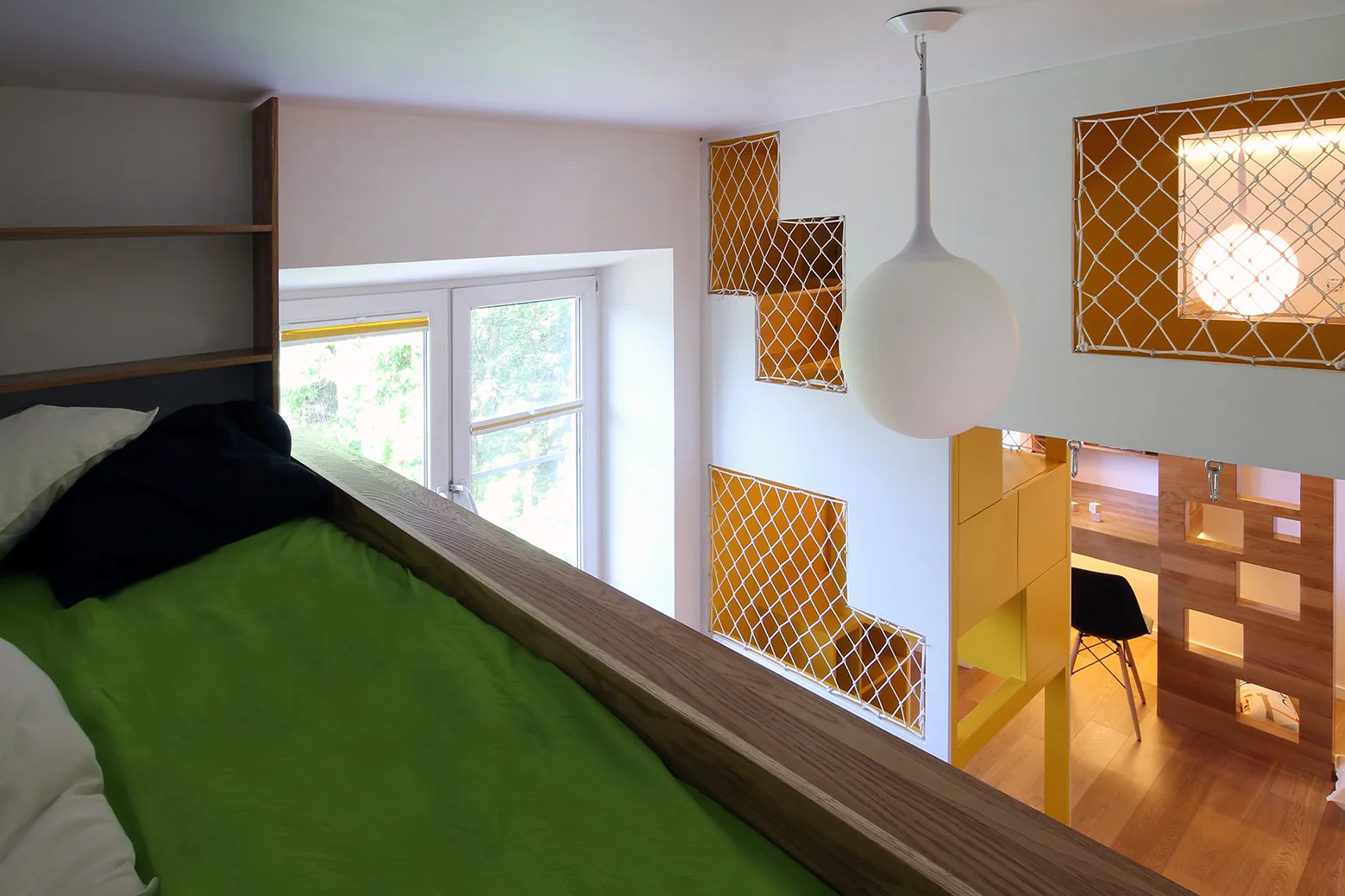 An elevated loft bed with green bedding sits near a wall featuring yellow recessed niches covered with rope netting above a built-in wooden desk.