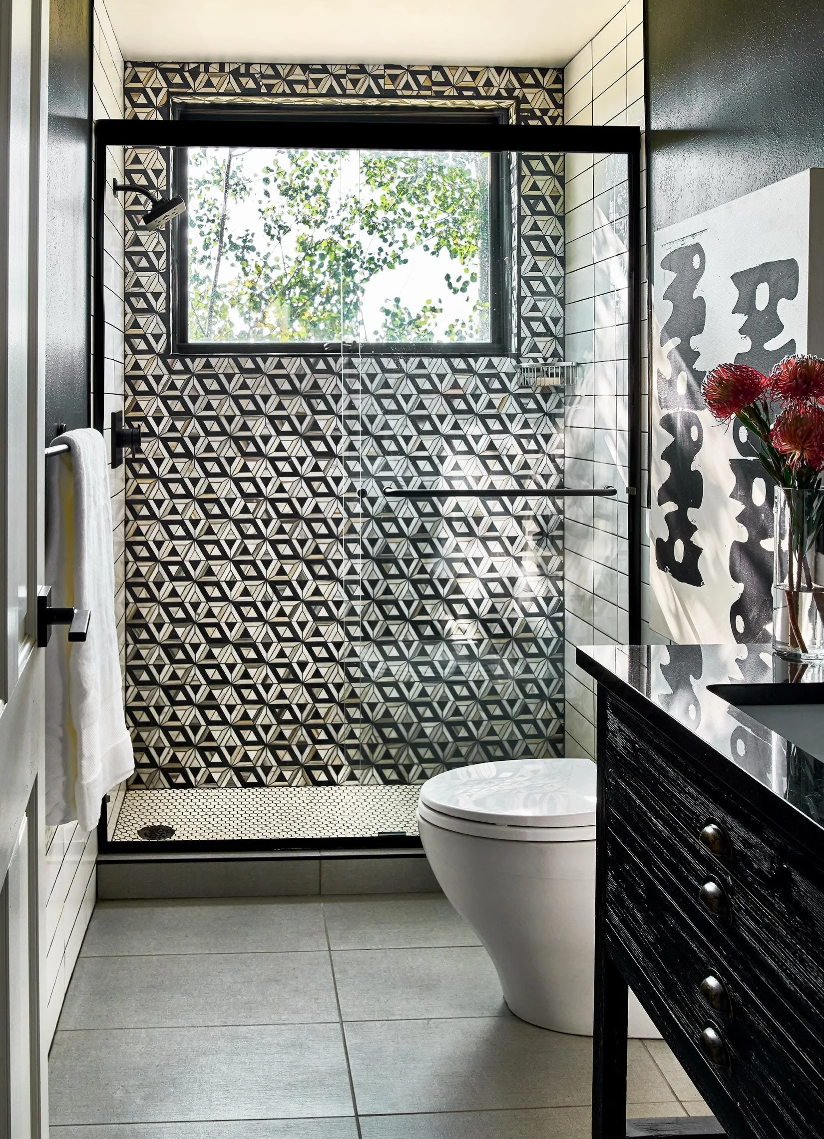 A modern bathroom showcases a shower with bold black and white geometric patterned wall tiles, a glass door, a toilet, and a dark vanity.