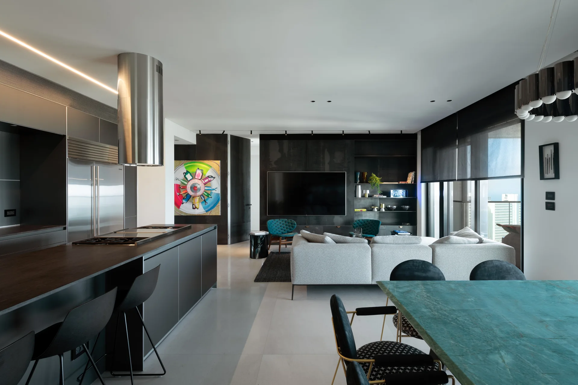 An open-plan apartment interior showing a dark kitchen island, a light grey sectional sofa, and a rectangular turquoise stone dining table.
