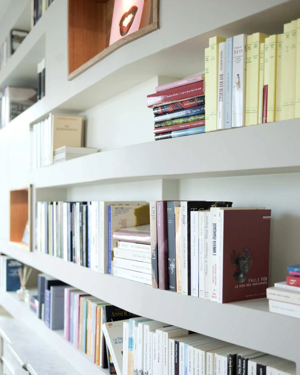 Modern off-white built-in bookshelves filled with colorful books, featuring recessed wooden accent niches.