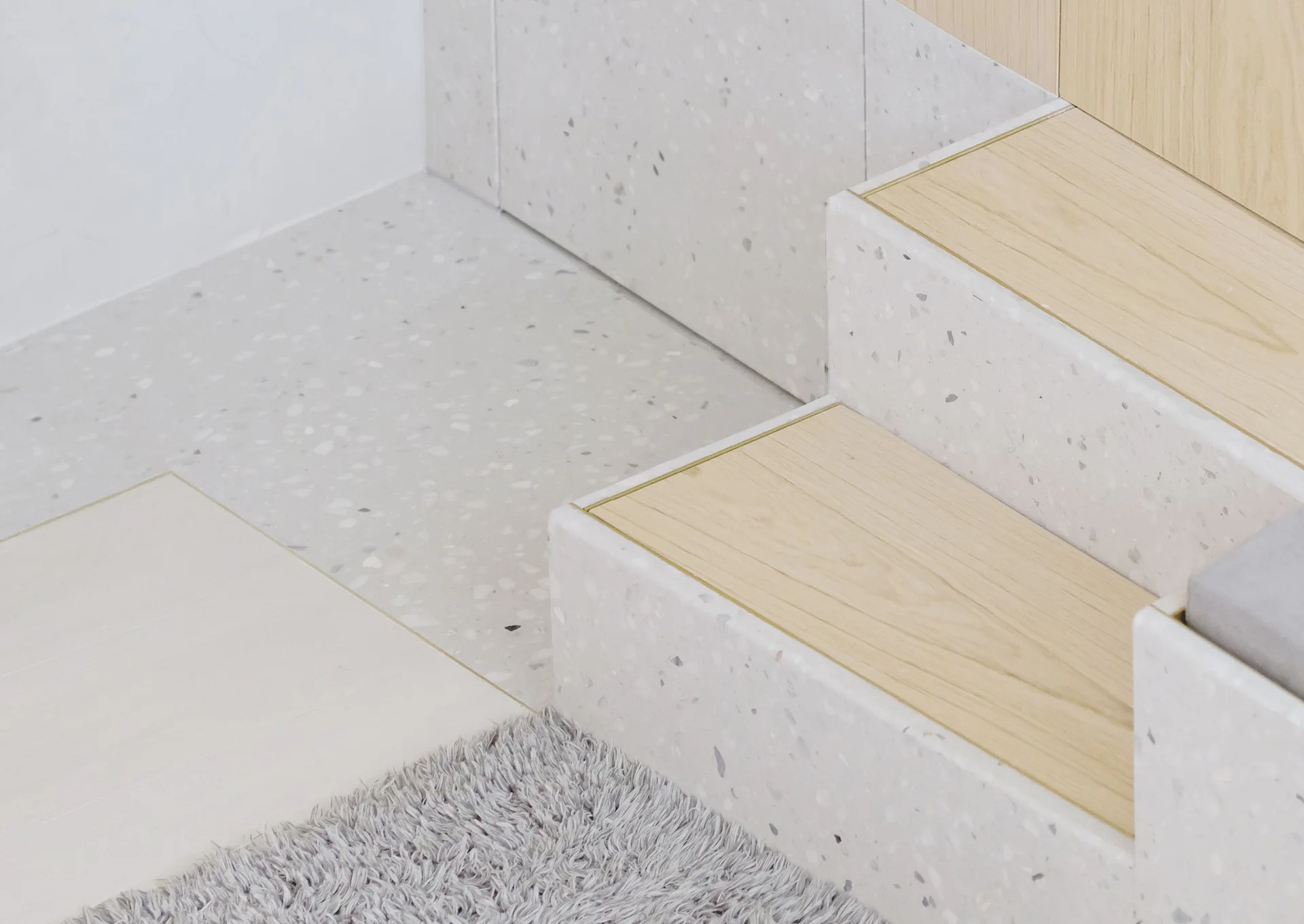 Close-up of a minimalist staircase featuring speckled white terrazzo risers, light oak wood treads, and gold metal edging.