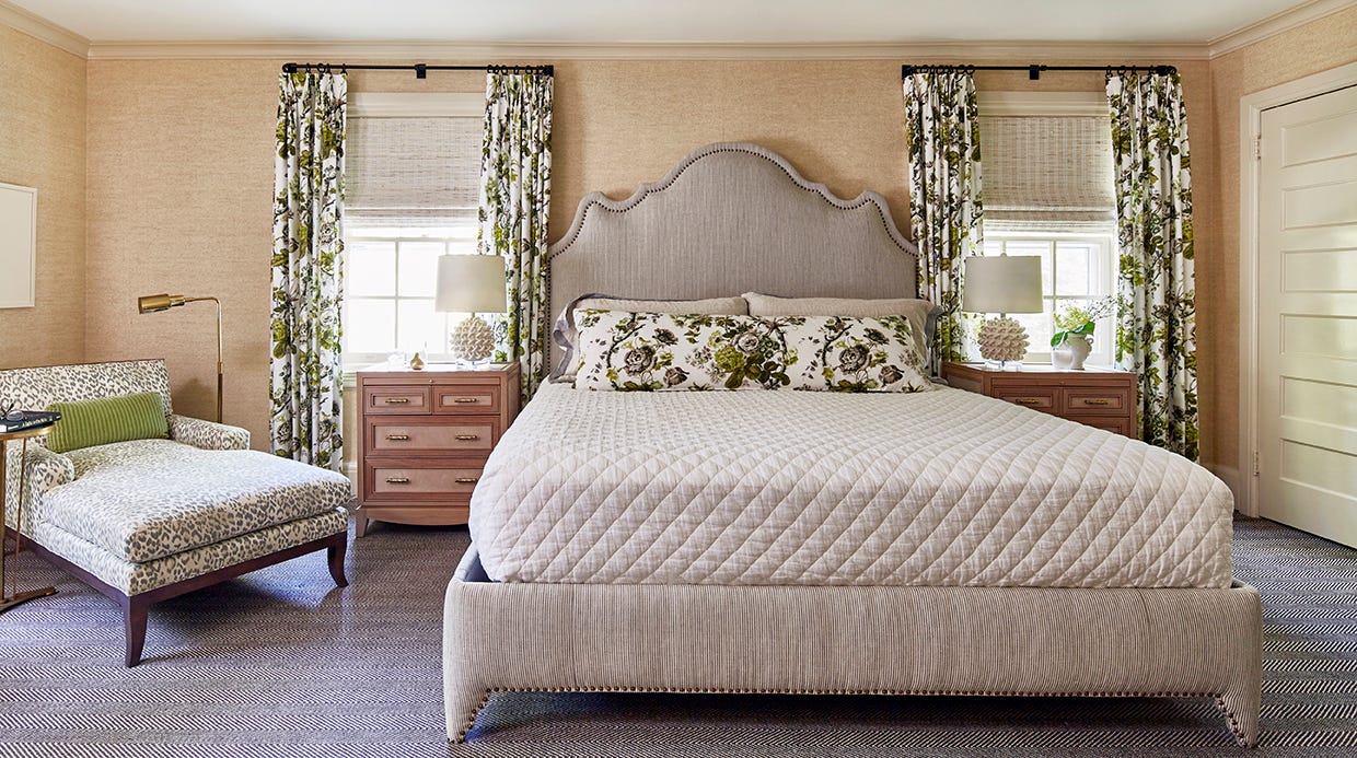 A traditional bedroom featuring an upholstered bed, floral patterned curtains, and a leopard print chaise lounge over a herringbone carpet.