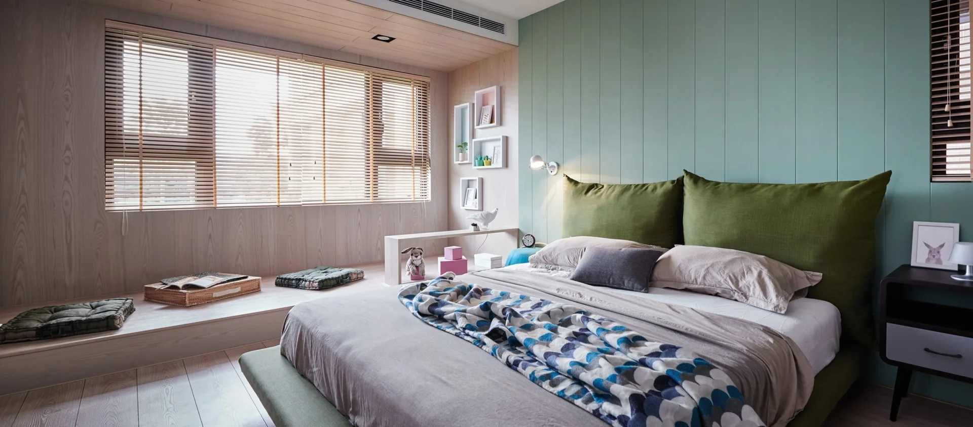 A minimalist bedroom features a low-profile bed against a mint green paneled wall and a raised wood platform with floor cushions by the window.
