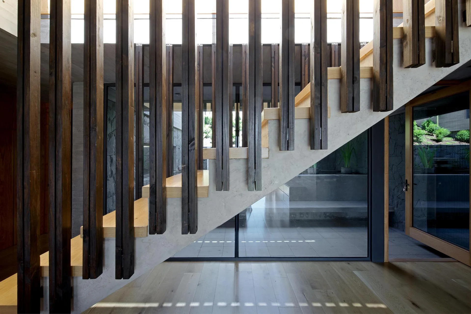 A modern staircase features light wood treads and a structural concrete base with vertical dark wood slats acting as a screen.