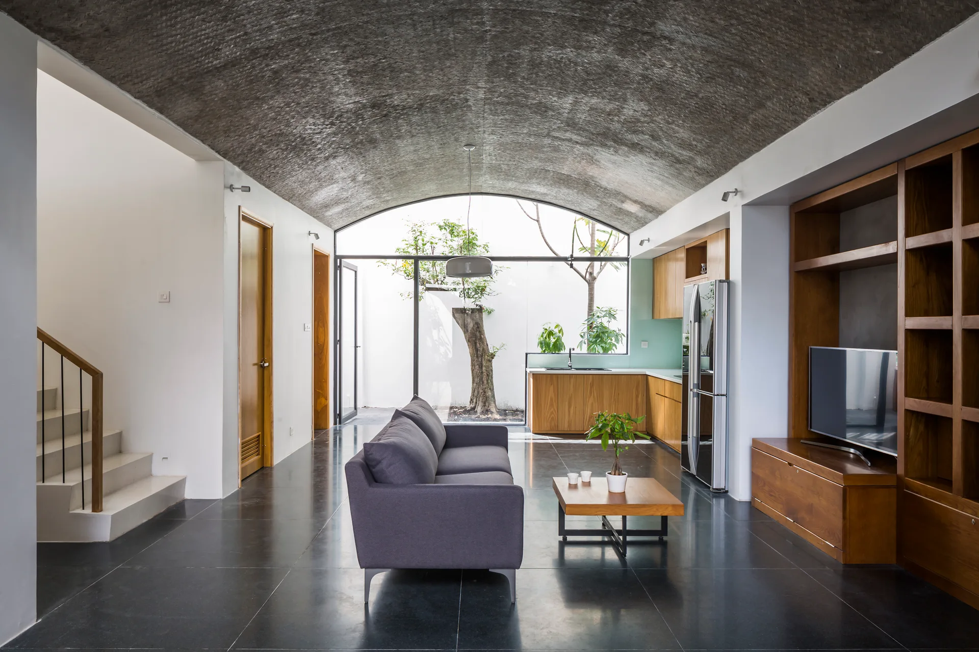 A modern living room with a grey sofa, wooden media unit, and a textured vaulted ceiling looking out onto an outdoor courtyard.