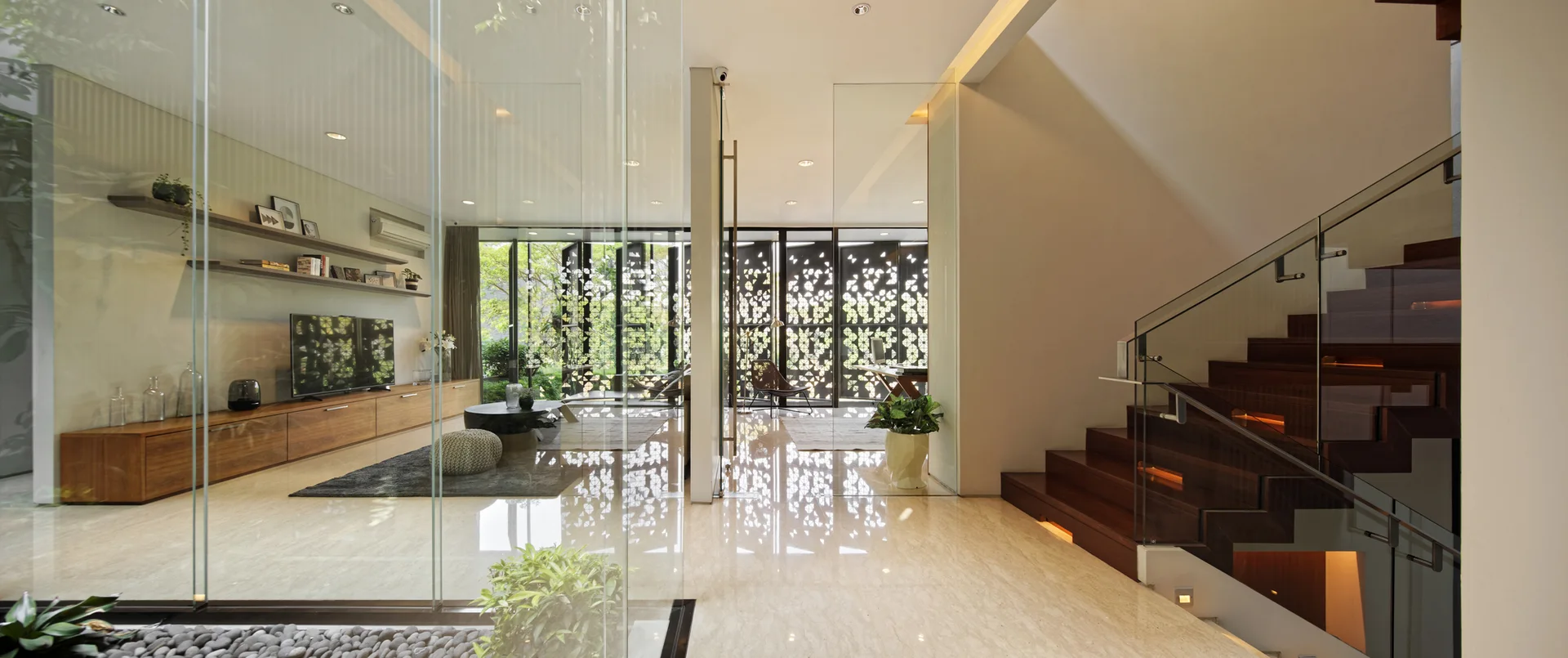 A modern open-plan home with polished stone floors, a dark wood staircase with glass railings, and transparent glass partition walls.