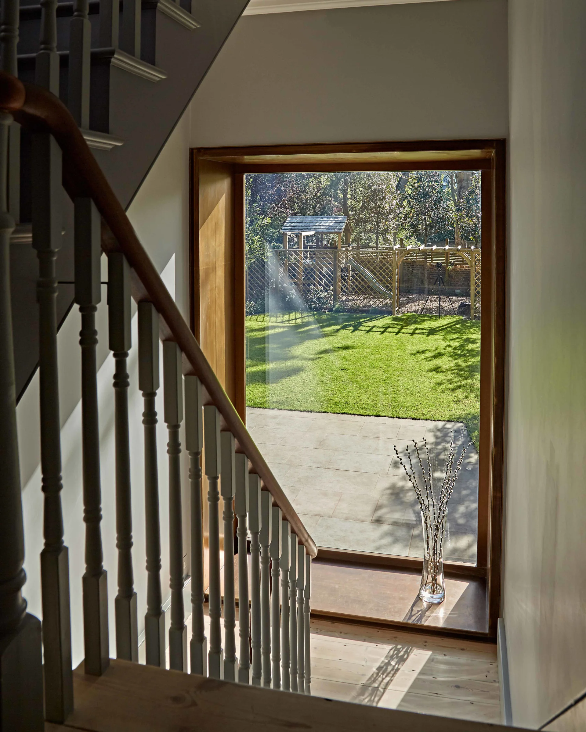 A traditional staircase landing features a wooden railing and a large wood-framed window looking out onto a green backyard with a play set.
