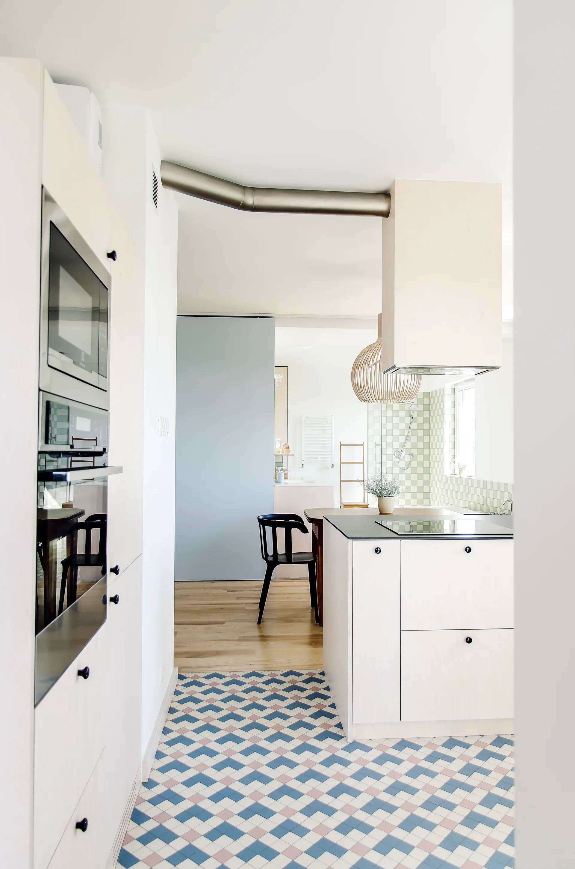 A Scandinavian kitchen features blonde wood cabinetry, a geometric pattern tiled floor in blue and white, and a pale blue sliding door in the background.