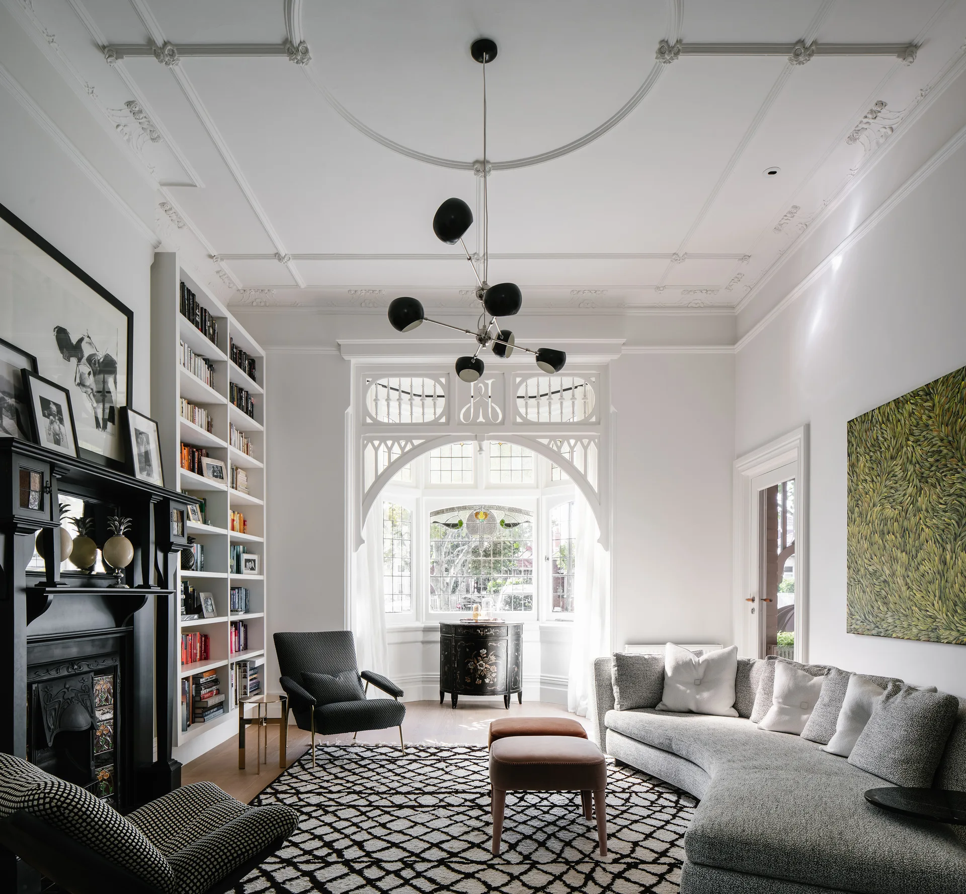 A transitional living room features a curved grey sofa, an ornate plaster ceiling, a black fireplace, and a built-in white bookshelf.