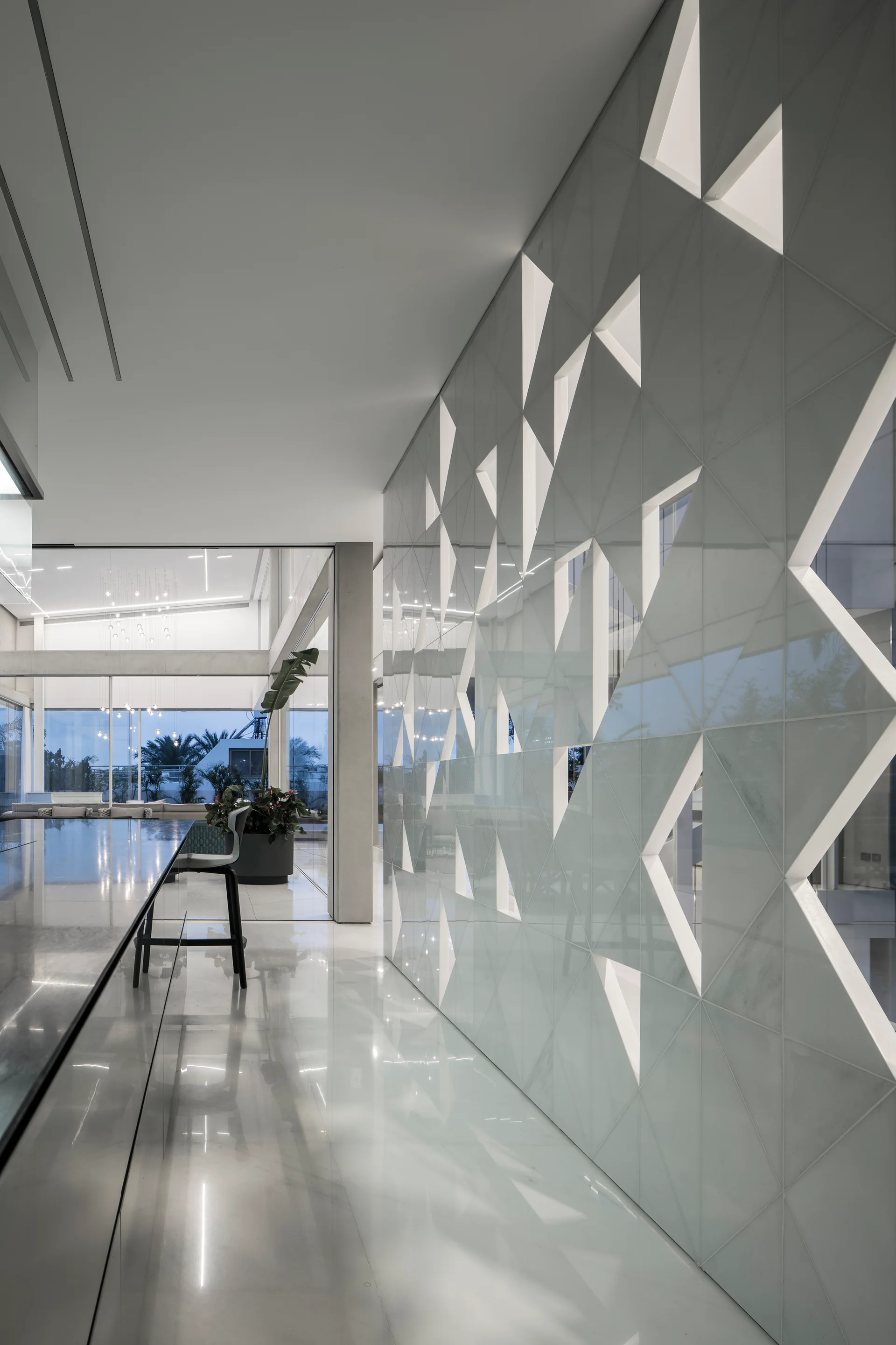 A modern minimalist kitchen features a reflective polished floor, a long grey island, and a tall white wall panel with triangular geometric cutouts.