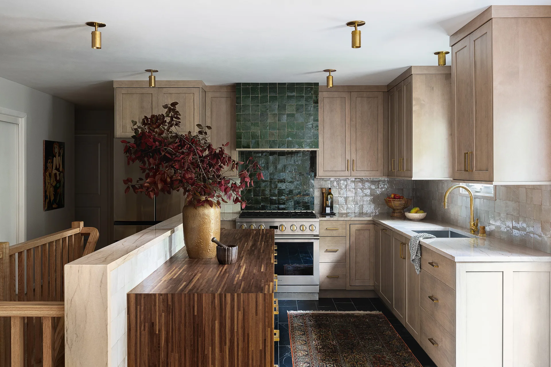 A modern residential kitchen with light wood cabinetry, a dark green tile backsplash, and a large wood-topped kitchen island.