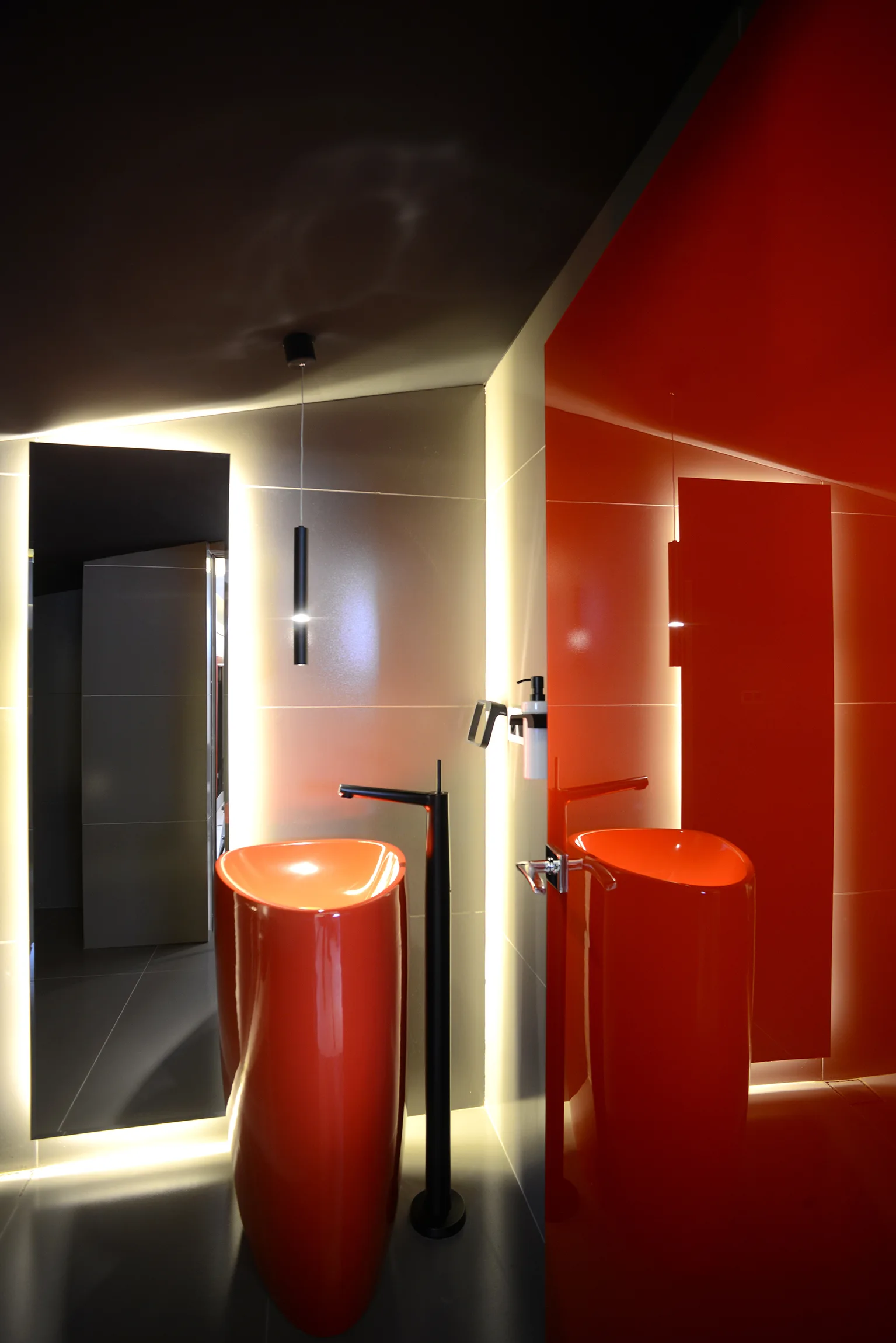 A minimalist bathroom featuring a glossy red pedestal sink, a black floor-mounted faucet, and wall panels backlit with soft LED strip lighting.