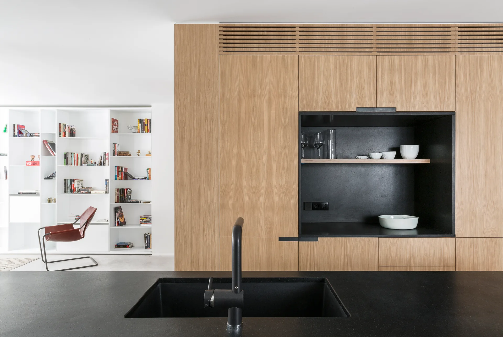 A modern kitchen featuring flat-panel wood cabinetry with an integrated matte black niche, positioned behind a black island with a dark sink.