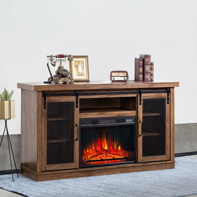 A rustic wood fireplace media console with sliding metal mesh doors sits on a blue rug, topped with vintage-style decor objects against a plain white wall.