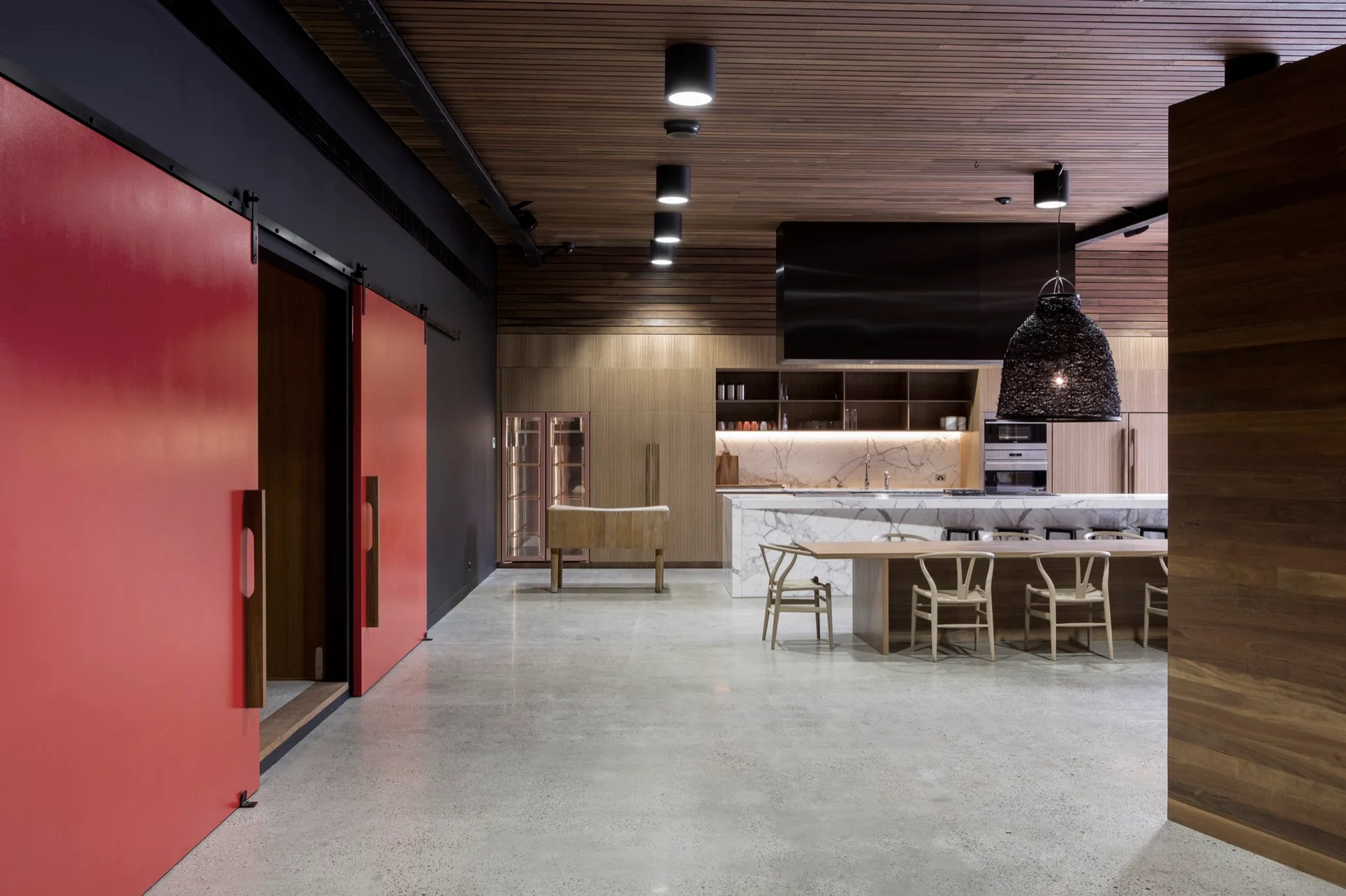 A modern kitchen and dining area with a marble island, wooden table, and large red sliding doors set against a dark wall.