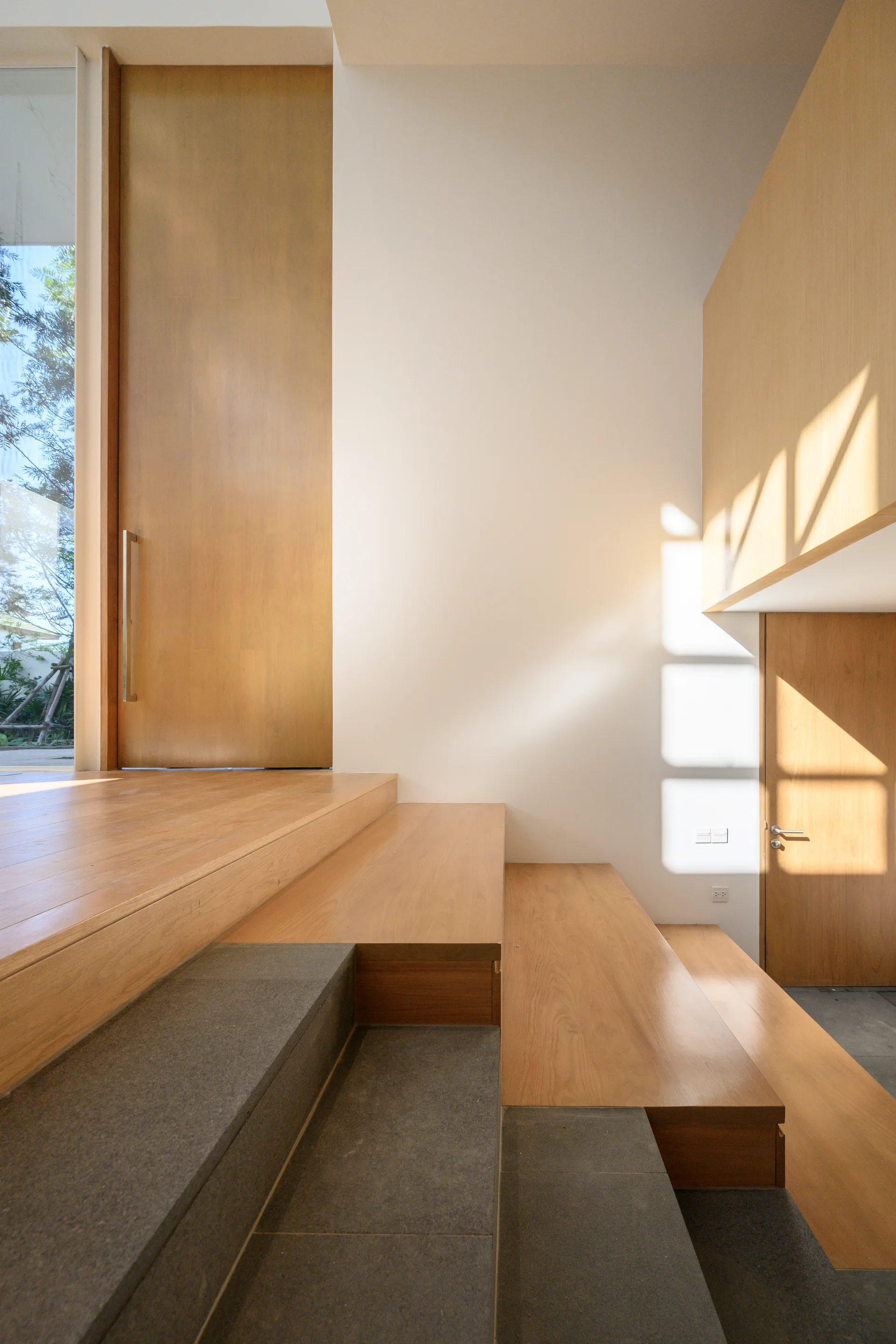 A multilevel staircase featuring light wood treads and dark grey stone steps leading to an elevated wooden landing with a tall wood door.