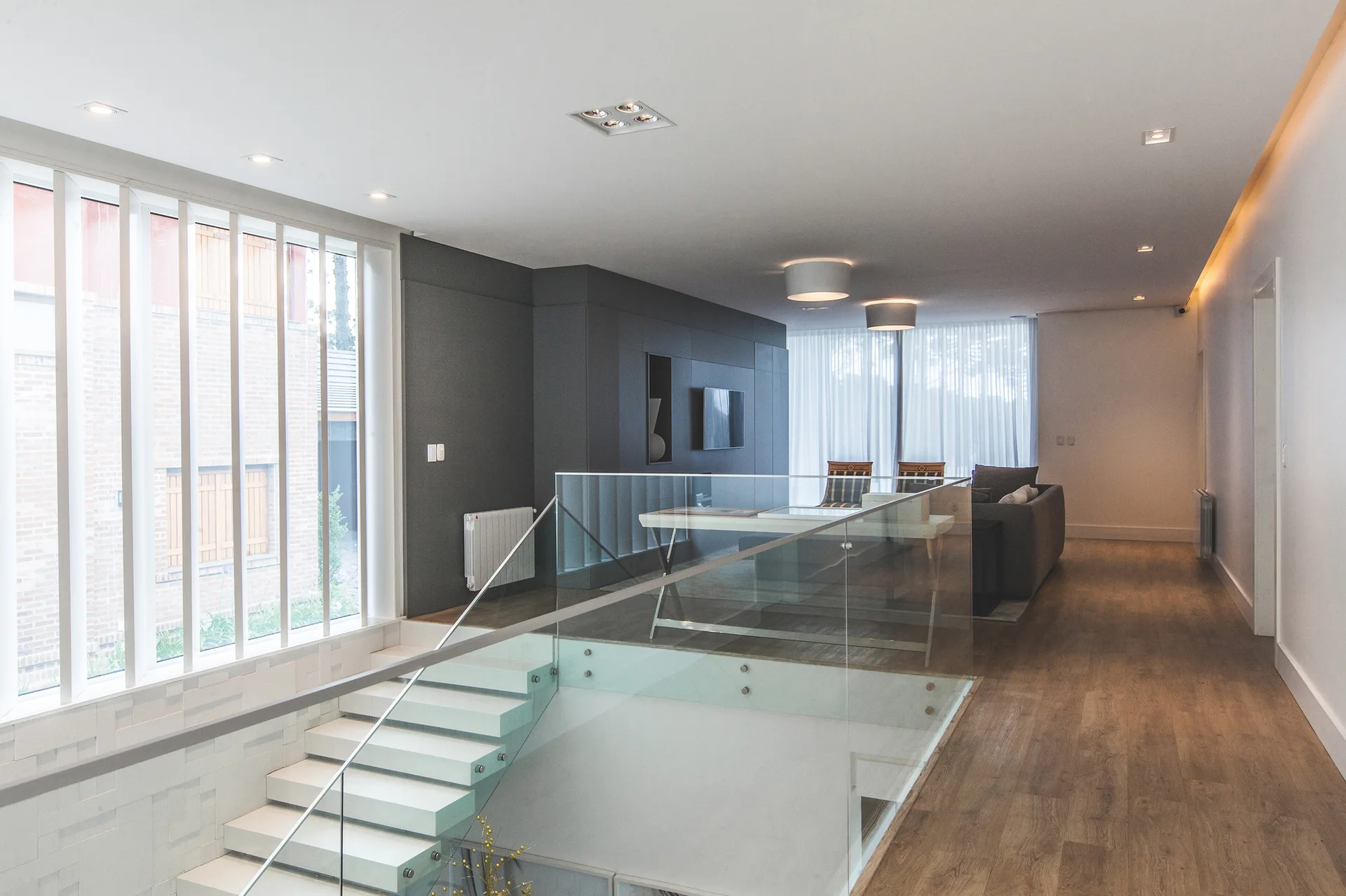 A modern interior featuring a white floating staircase with a glass railing, a dark grey paneled accent wall, and wood flooring.