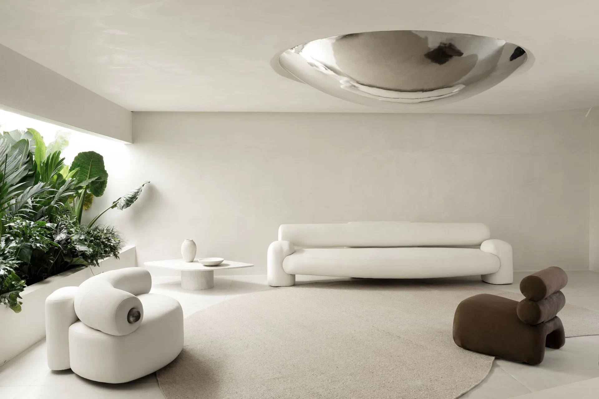 A minimalist cream living room featuring curved sculptural furniture, a round rug, an integrated planter with green plants, and a mirrored ceiling dome.