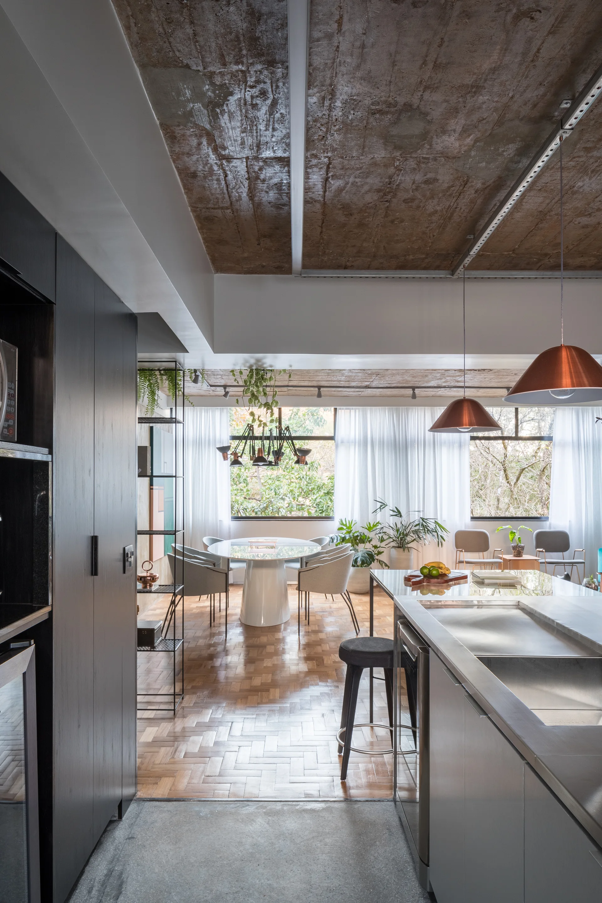 An open-concept kitchen and dining space featuring an exposed concrete ceiling, a stainless steel island, parquet wood flooring, and a white round table.
