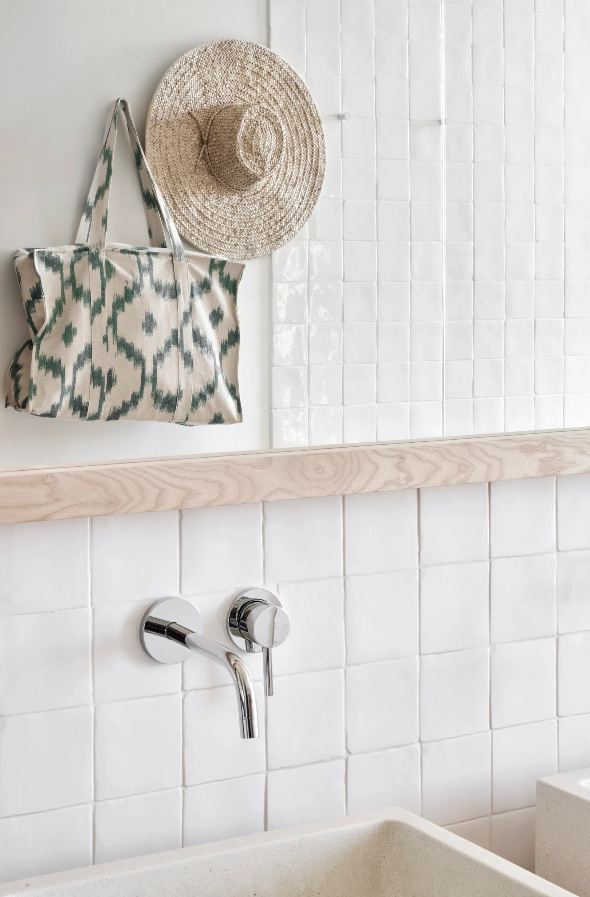 A close-up of a bathroom vanity featuring a wall-mounted chrome faucet, a stone sink, and a glossy white tiled backsplash with a wood ledge.