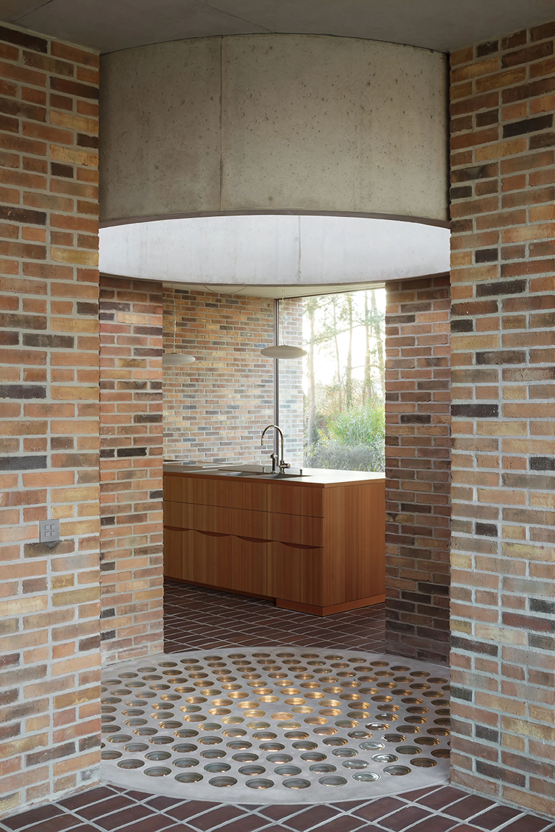 A wood kitchen island sits framed by exposed brick walls, a curved concrete ceiling arch, and a floor featuring circular glass block inlays.