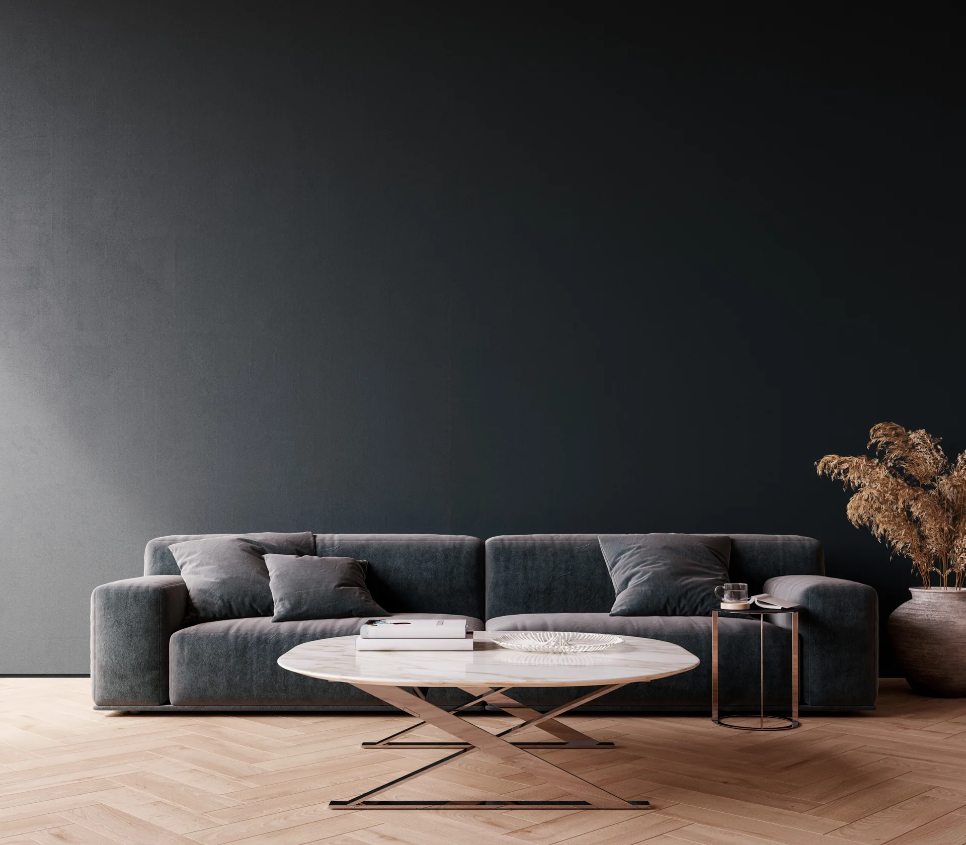 A grey upholstered sofa sits against a dark charcoal wall on a light wood herringbone floor with a round marble coffee table.