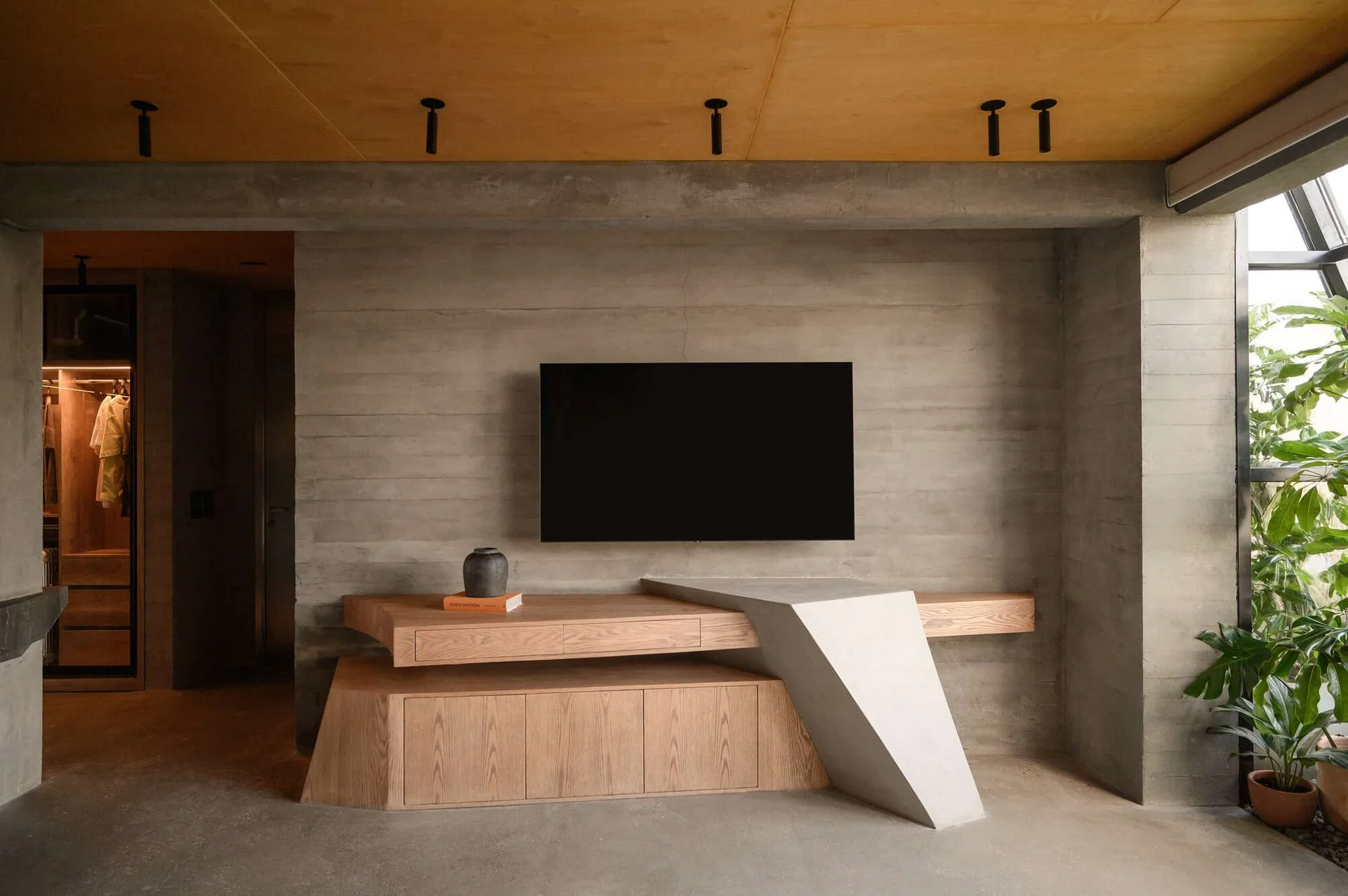 A minimalist living room with a custom wood and concrete media console against a board-formed concrete wall.