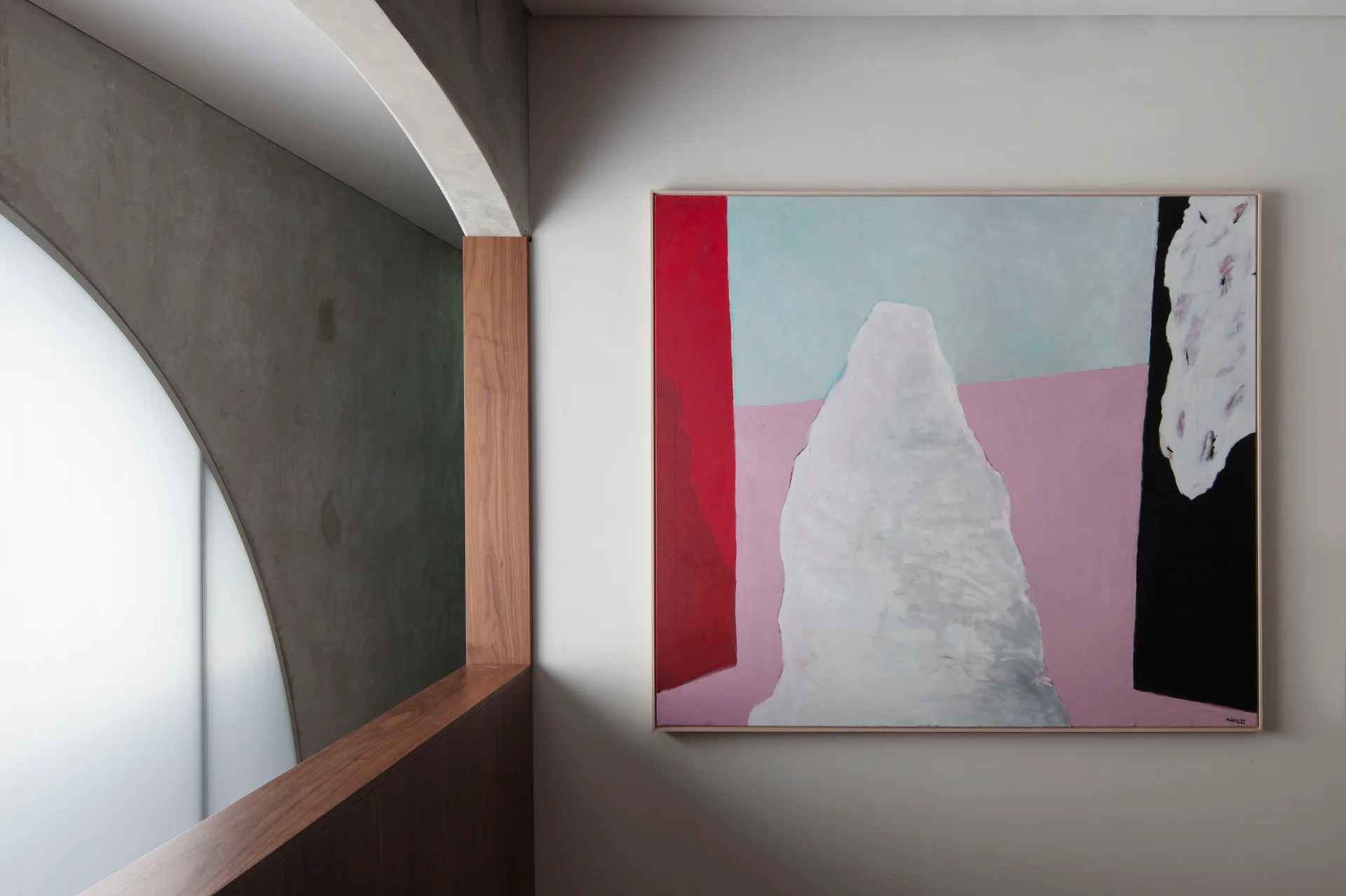 A large abstract painting hangs on a light grey wall next to a concrete archway with a wood ledge and frosted glass window.