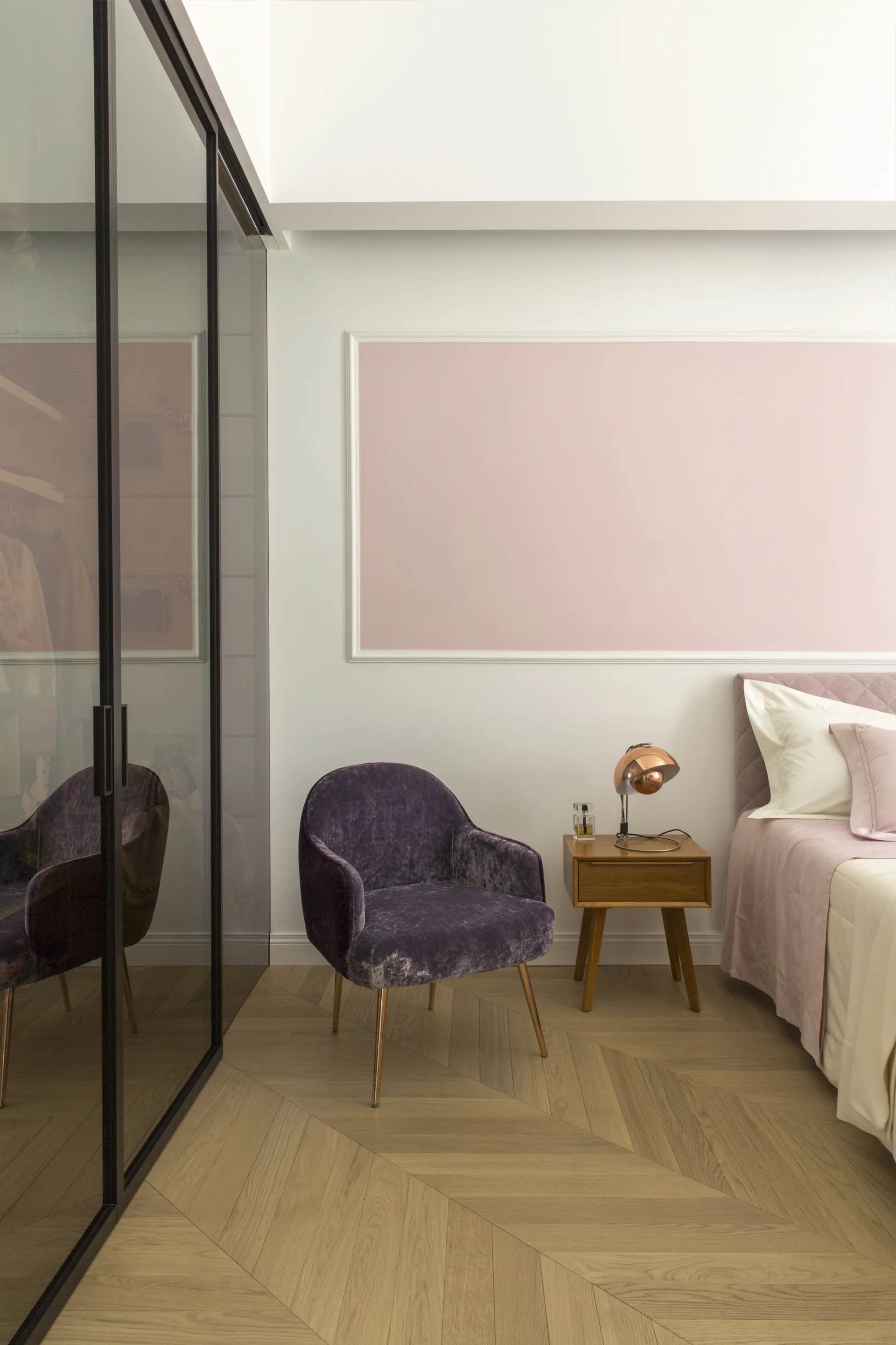A modern bedroom features a purple velvet armchair beside a wood nightstand, a pink wall molding panel, and dark reflective wardrobe doors.