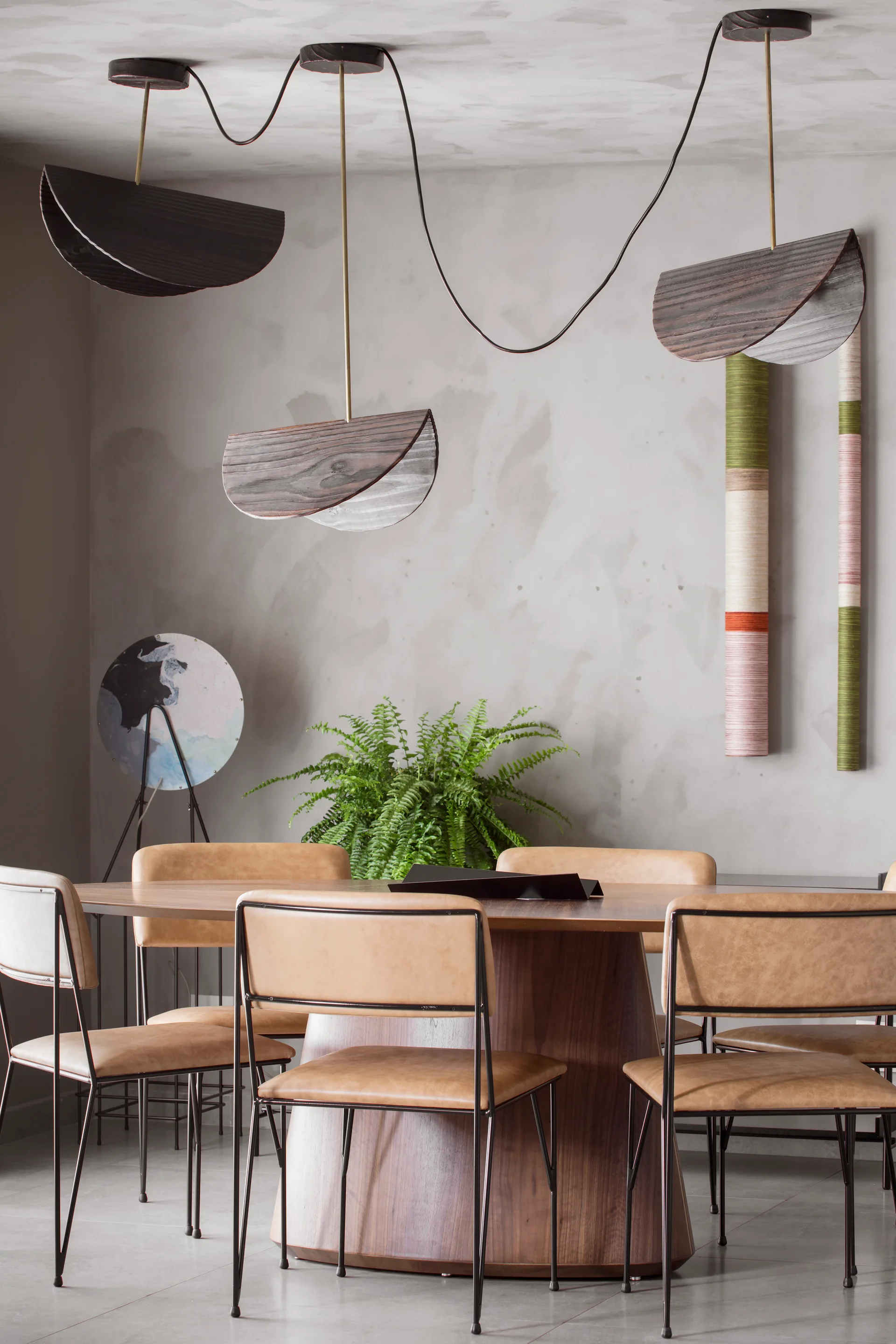 A contemporary dining room with a round wooden table, tan chairs, and sculptural curved pendant lights against a mottled grey plaster wall.