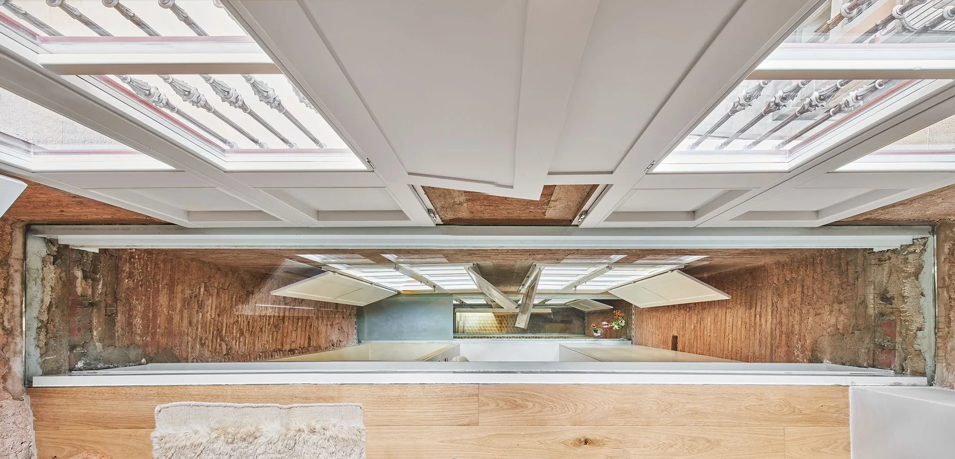 A top-down view through a floor cutout shows white painted beams above exposed brick walls and a lower kitchen area.