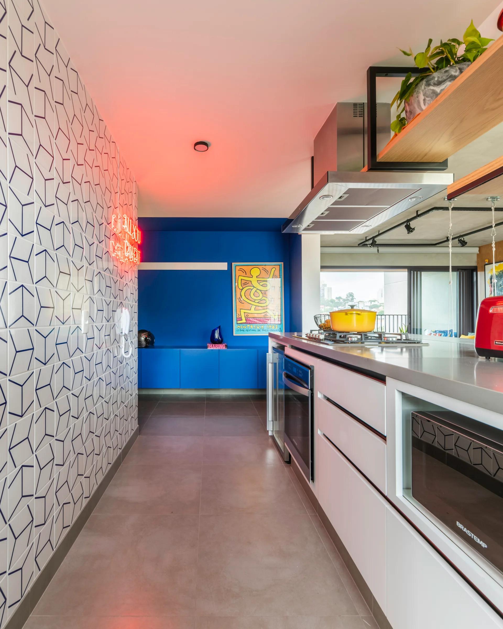 A modern kitchen hallway features a blue accent wall, a geometric tiled wall with a neon sign, and a grey tile floor.
