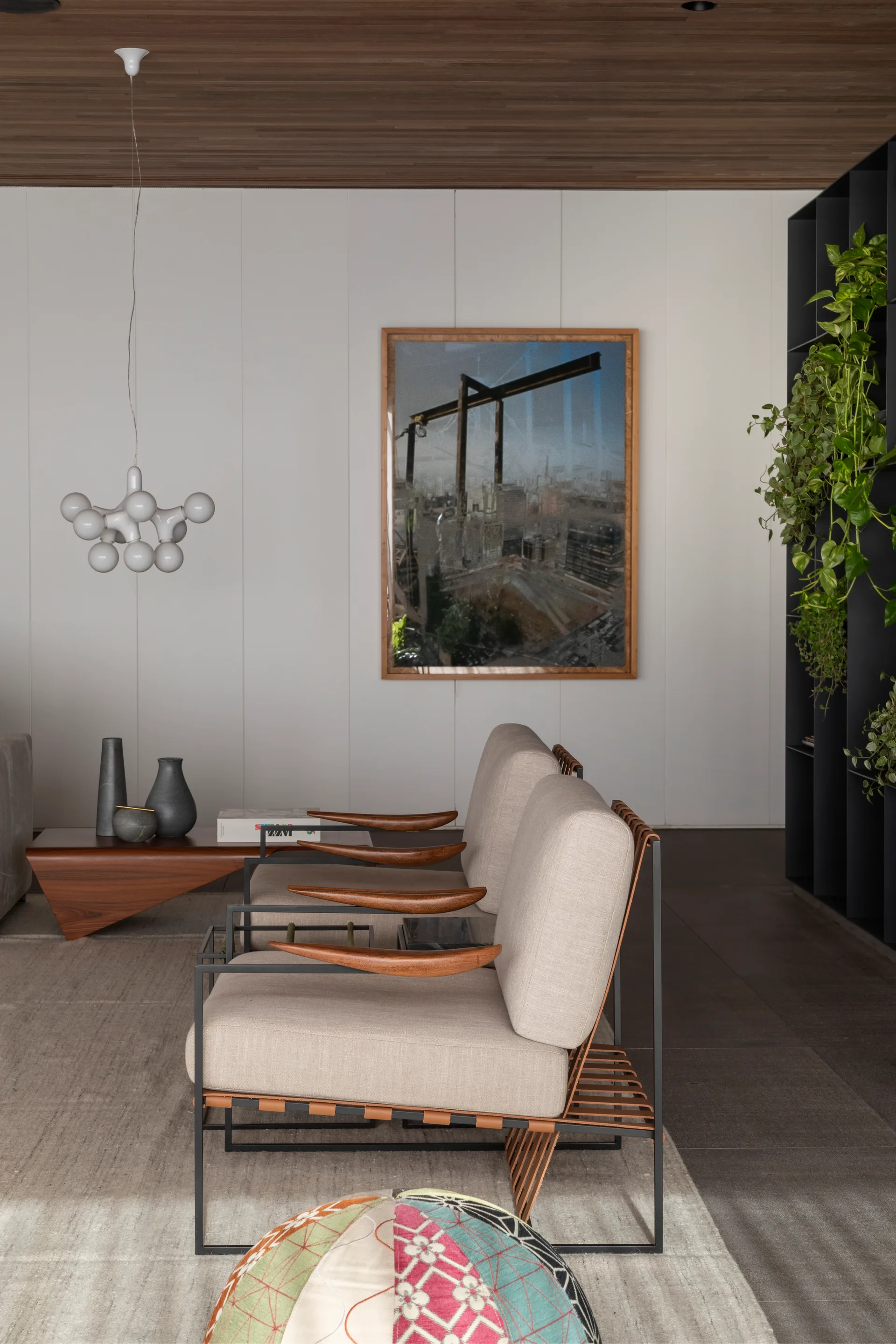Two beige lounge chairs with wooden armrests stand on a light grey area rug beneath a dark wood paneled ceiling and white walls.