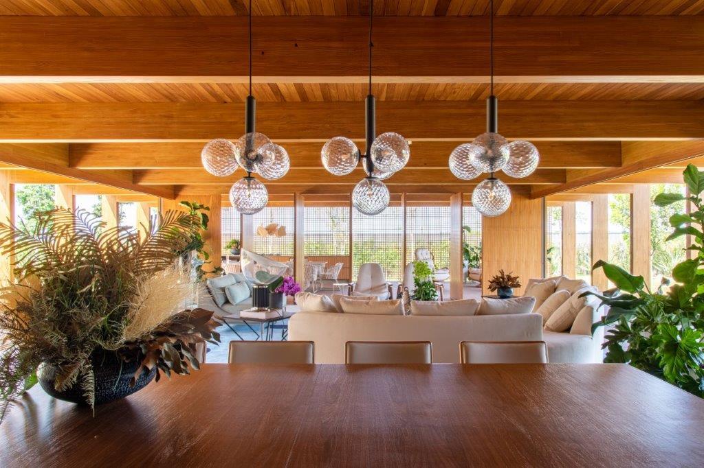An open living and dining area with an exposed wood ceiling, three spherical glass pendant lights, a cream sofa, and a wood dining table.