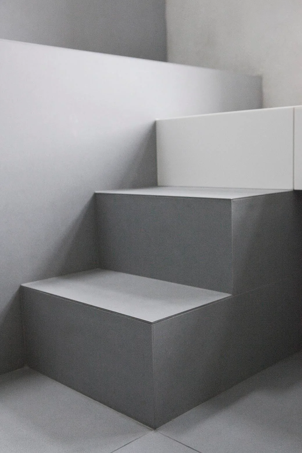 Minimalist grey staircase featuring sharp angular steps and a smooth matte finish on the stairs and surrounding walls.