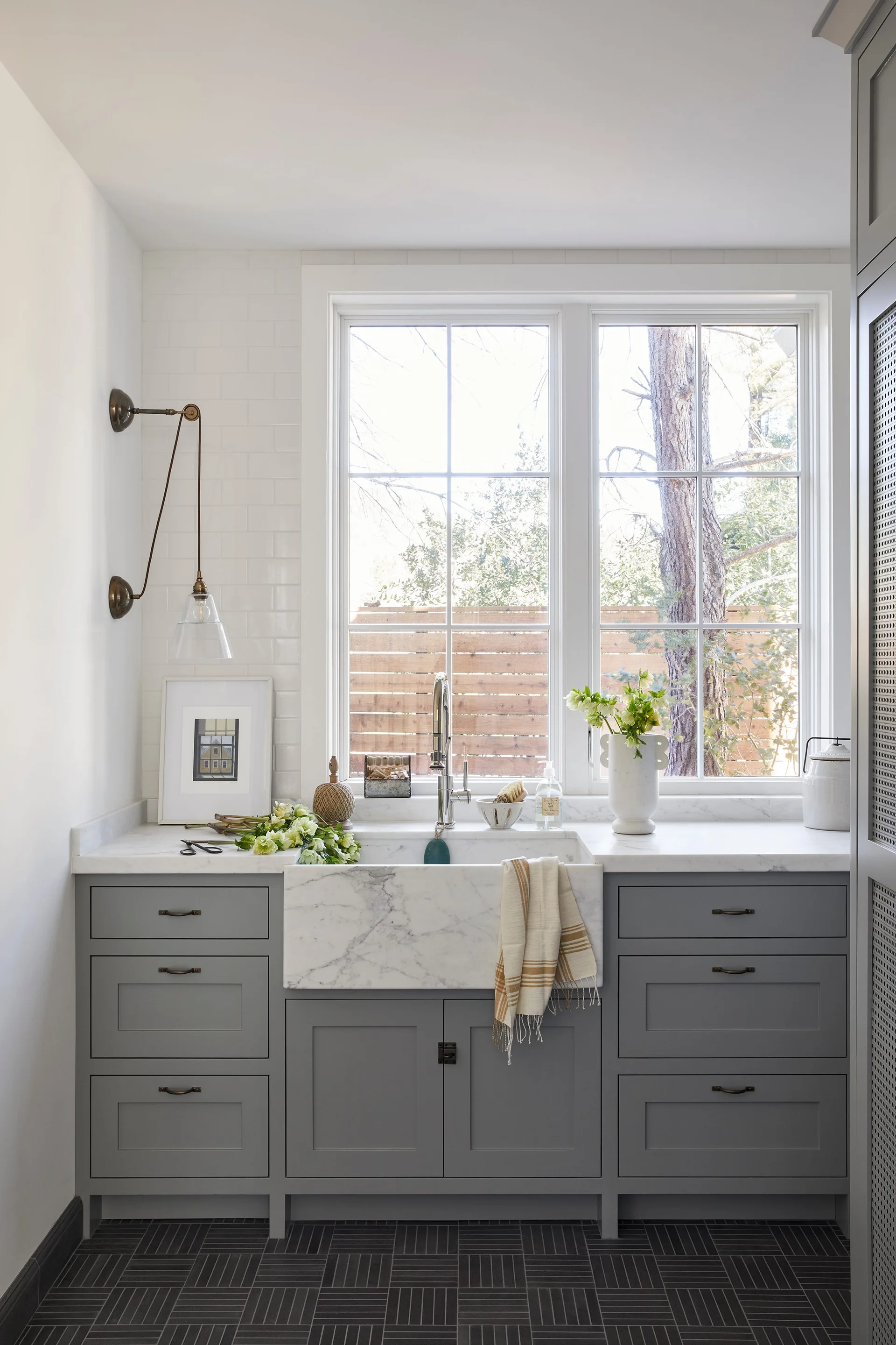 A utility room features grey cabinets, a marble apron-front farmhouse sink under a double window, and a dark tiled floor.