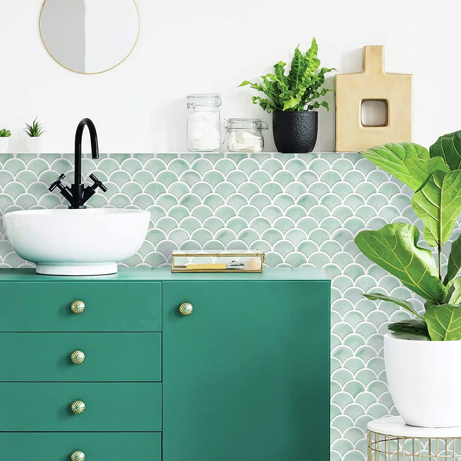 A green bathroom vanity cabinet features a white vessel sink and black faucet set against a green scalloped tile backsplash.