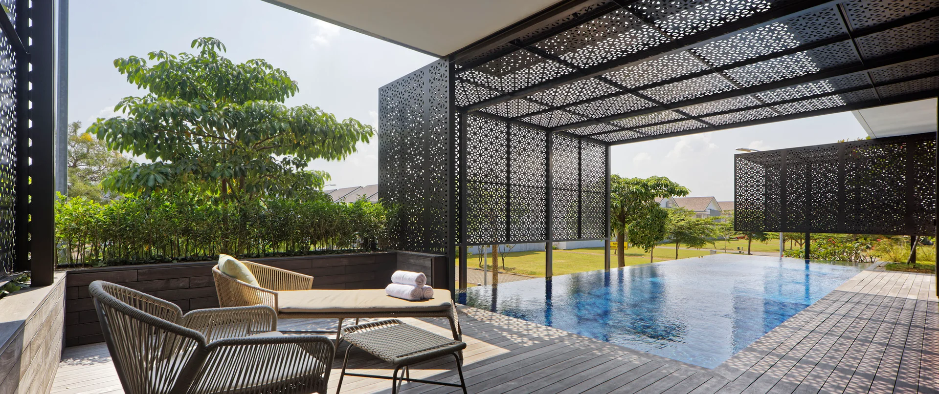 An outdoor pool deck features woven lounge furniture next to an infinity-edge swimming pool beneath geometric black metal privacy screens.