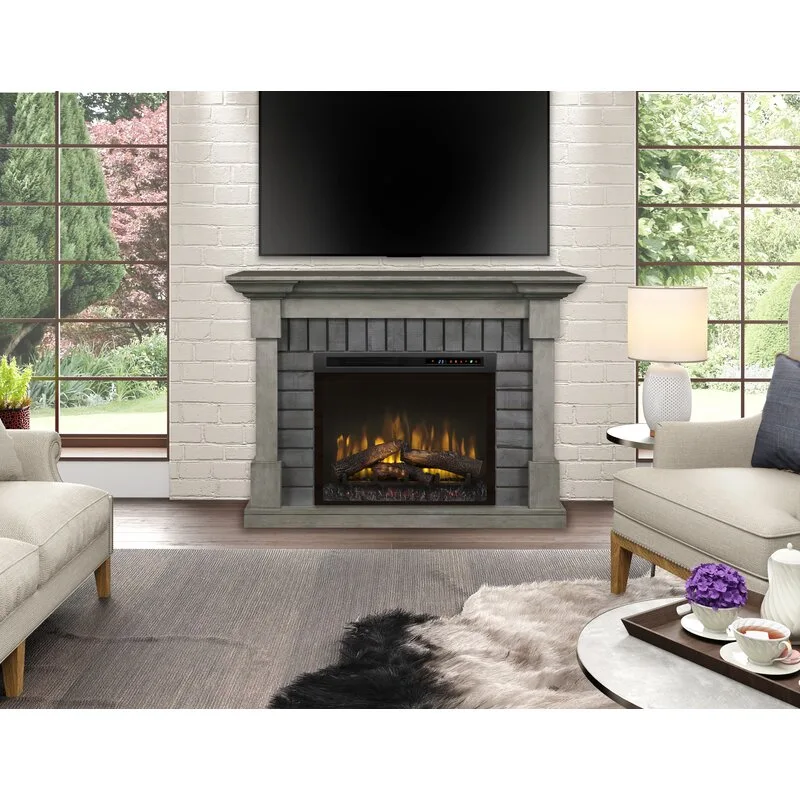 A living room featuring a central gray stone fireplace with a television mounted on a white brick wall, flanked by windows and neutral-toned sofas.