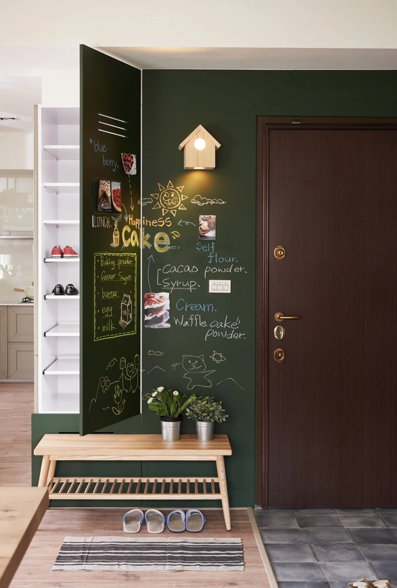 An entryway mudroom features a dark green chalkboard wall, a wooden bench with a slatted shelf, a tall open shoe cabinet, and a dark brown door.