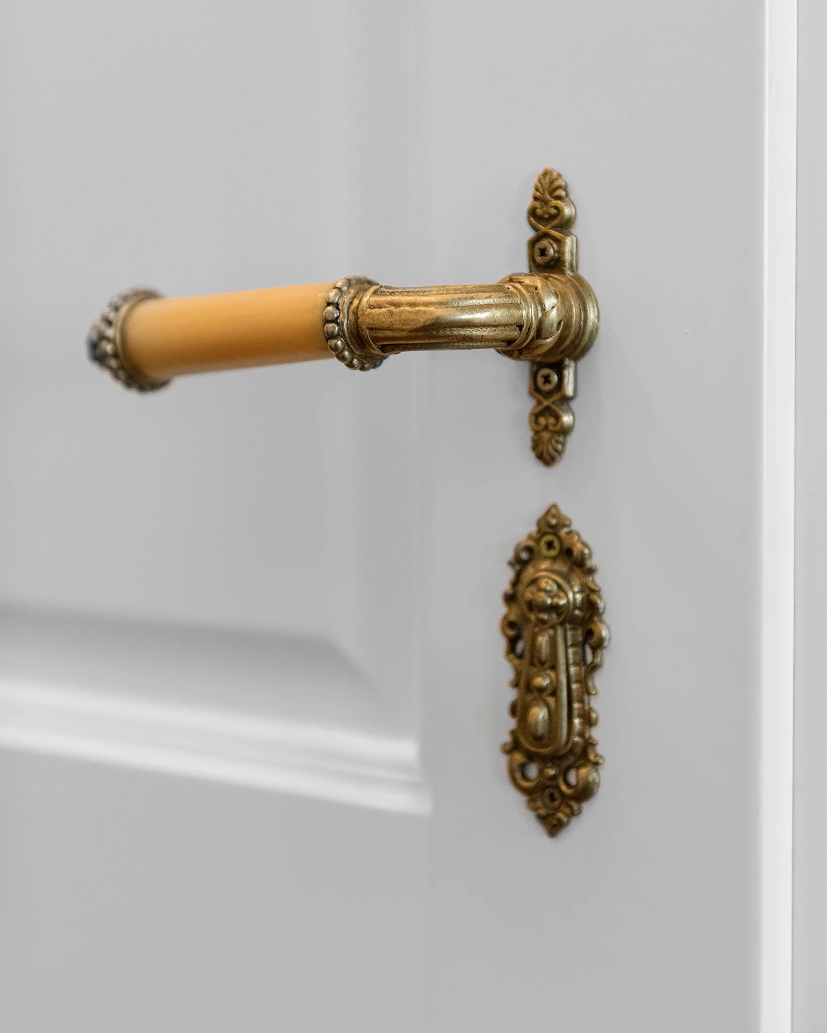 Close-up of an ornate brass door handle with a cream grip and matching decorative keyhole escutcheon on a white door.