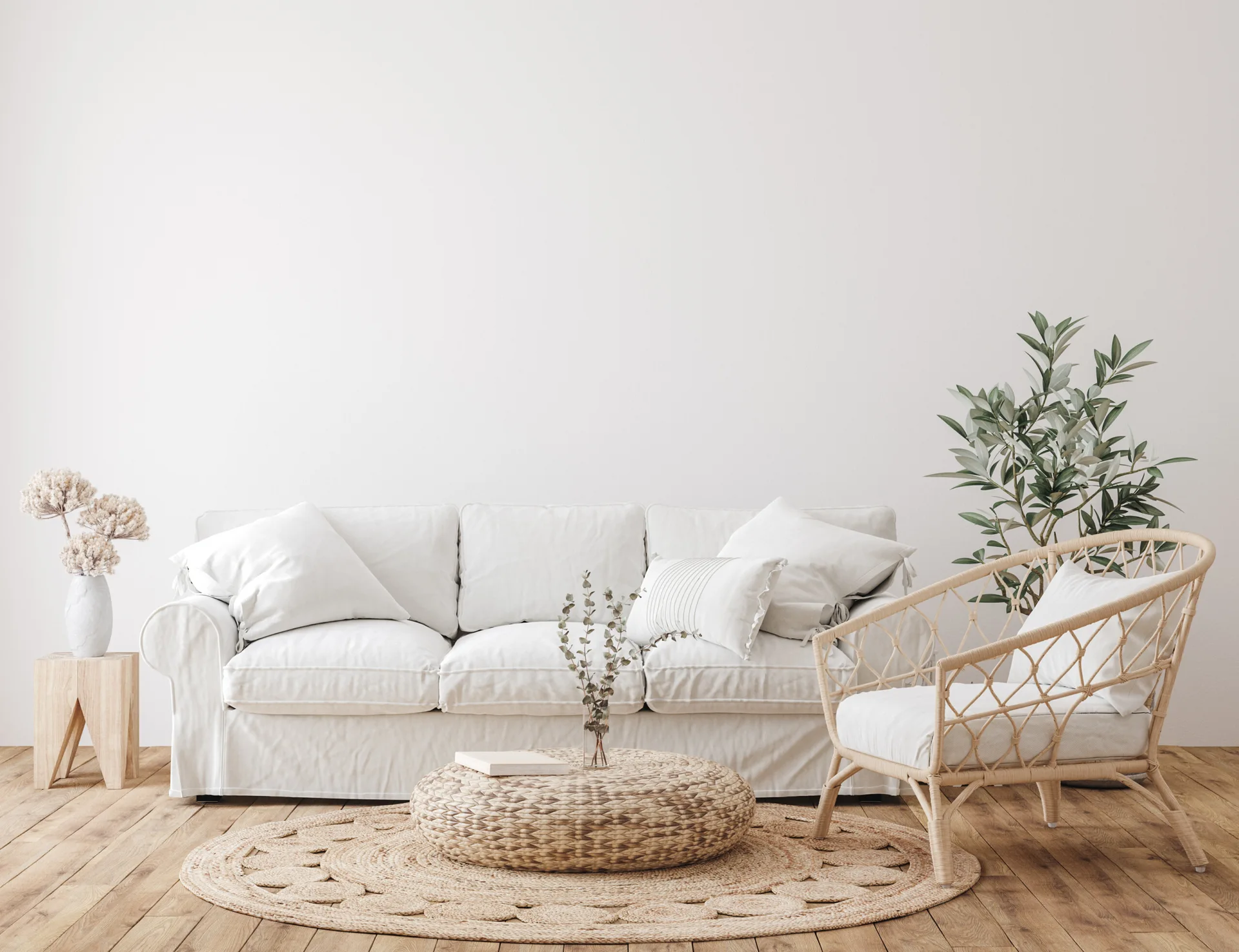 A white slipcovered sofa and a rattan armchair sit around a round woven coffee table on a circular jute rug against a plain white wall.