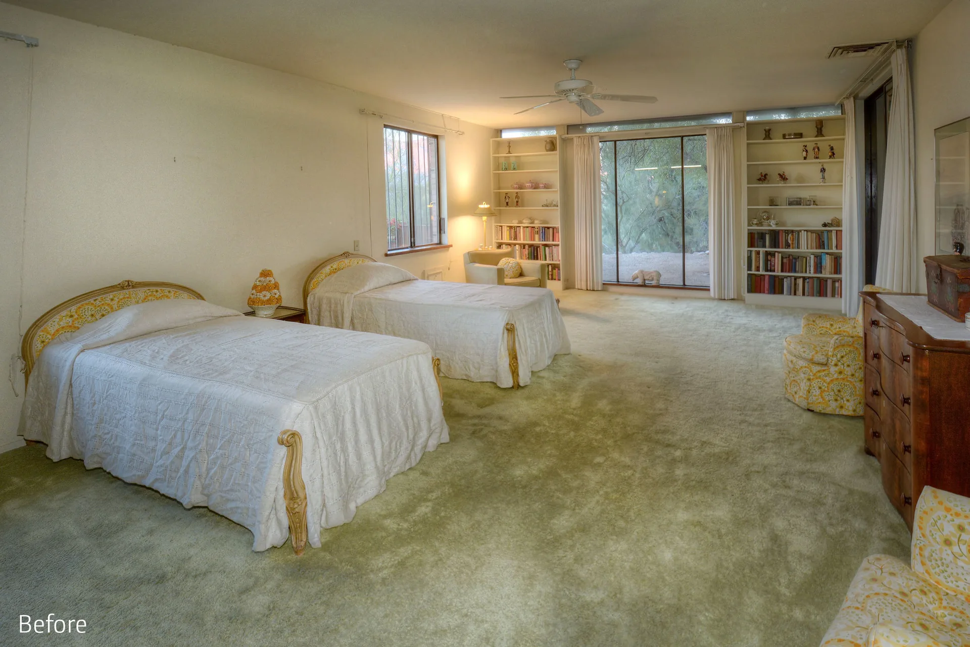 A vintage bedroom featuring two twin beds with white covers, sage green carpeting, and built-in bookshelves flanking a large window.