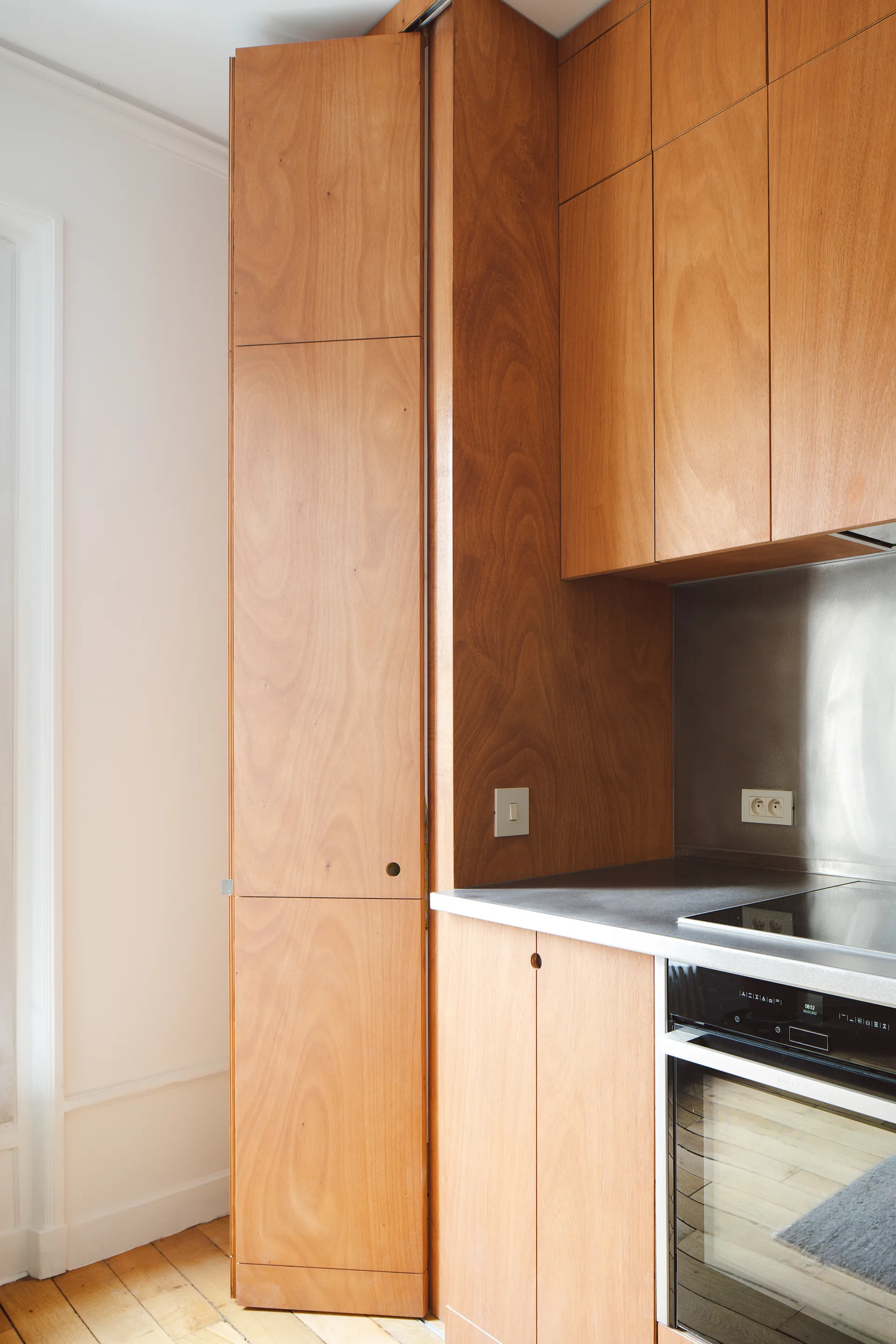 Minimalist kitchen corner featuring flat-panel wood cabinets, a folding pantry door, a built-in oven, and a metal backsplash.