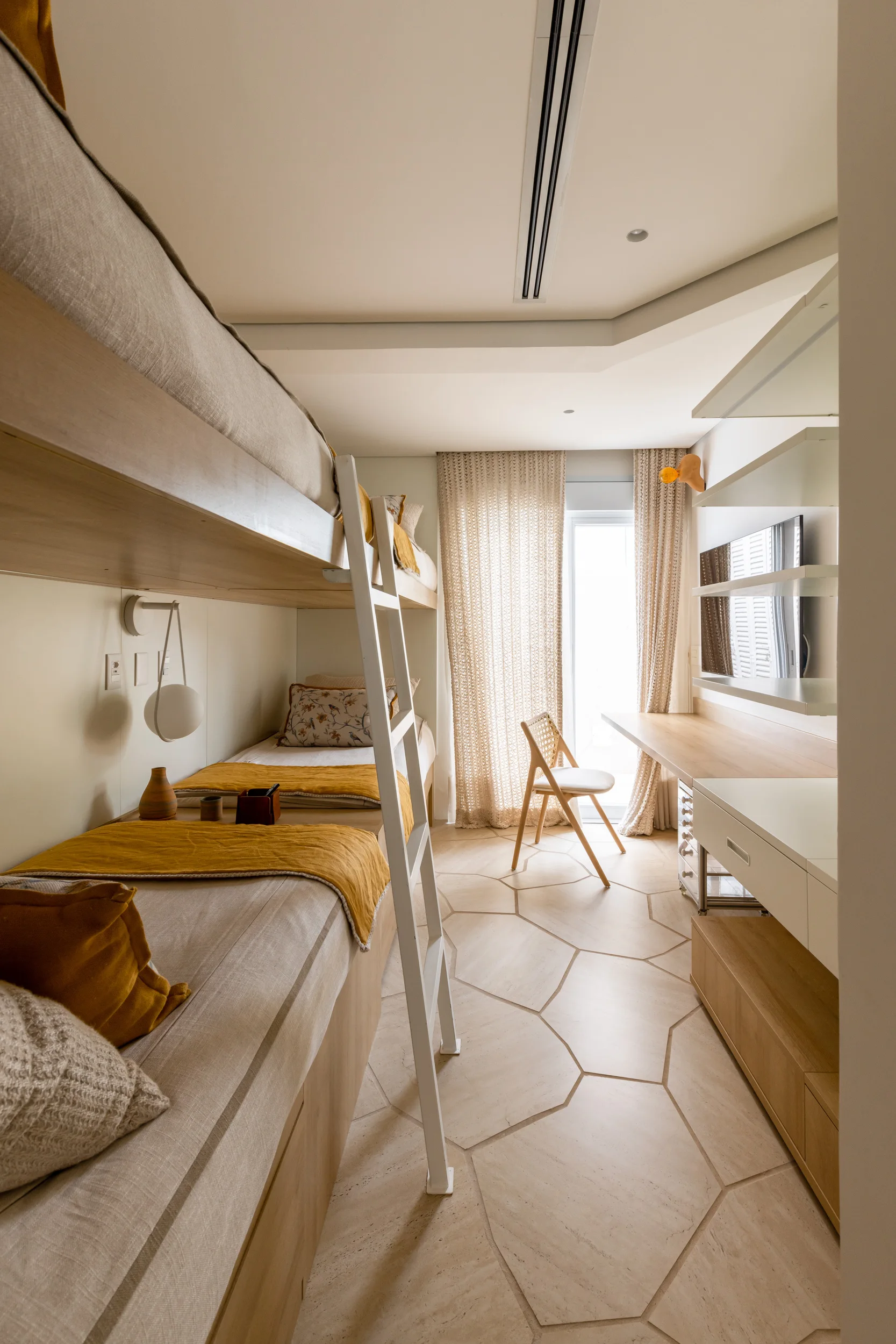 A minimalist bedroom featuring built-in light wood bunk beds with yellow blankets, a long study desk, and hexagonal floor tiles.