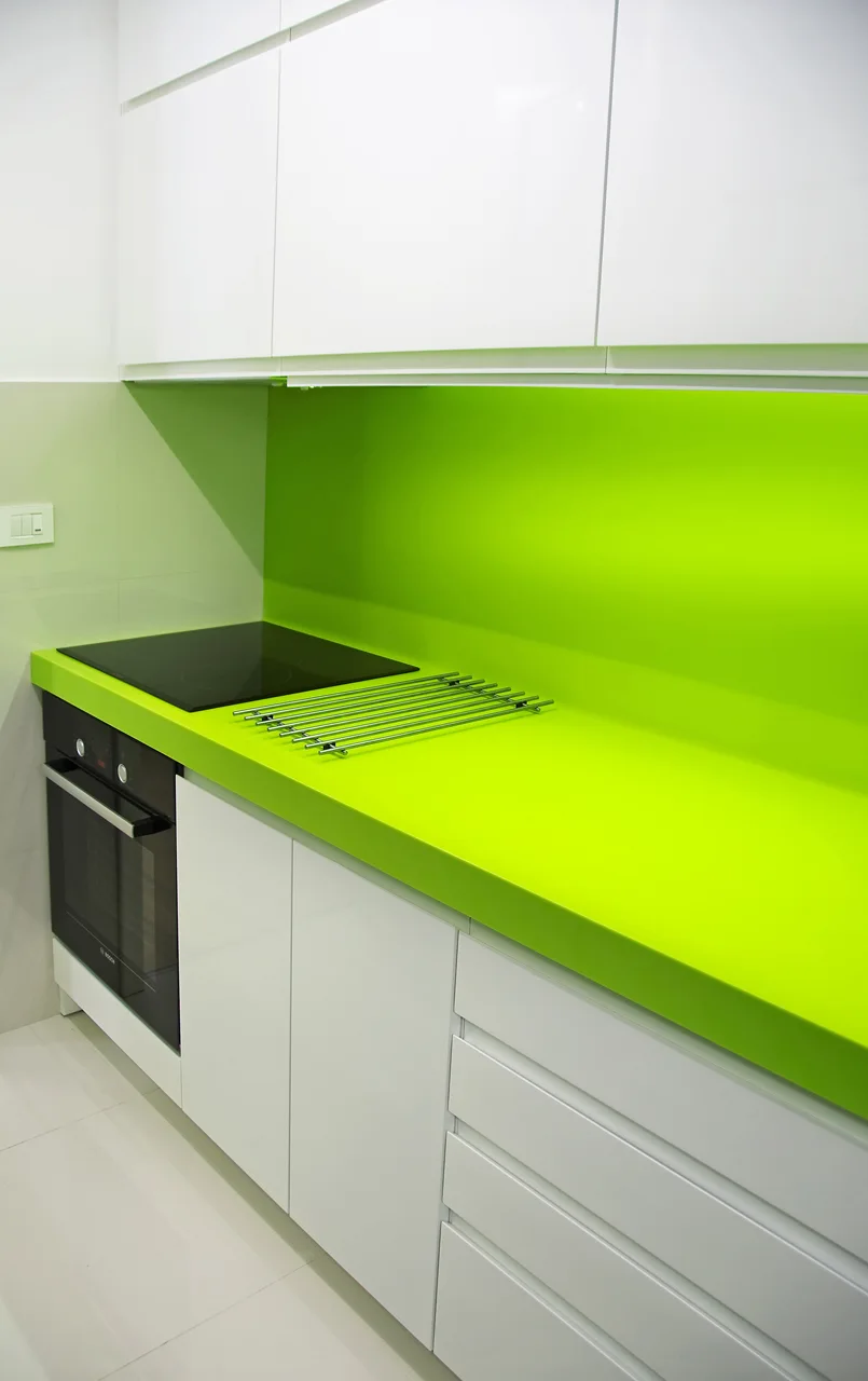 A modern kitchen featuring high-gloss white cabinets, a bright lime green countertop and matching backsplash, and an integrated black oven.