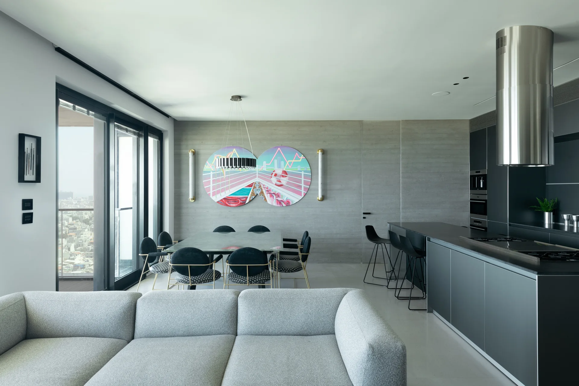 A modern open-plan living and dining area featuring a light gray sofa, dark kitchen island, and a textured gray wall with circular art.
