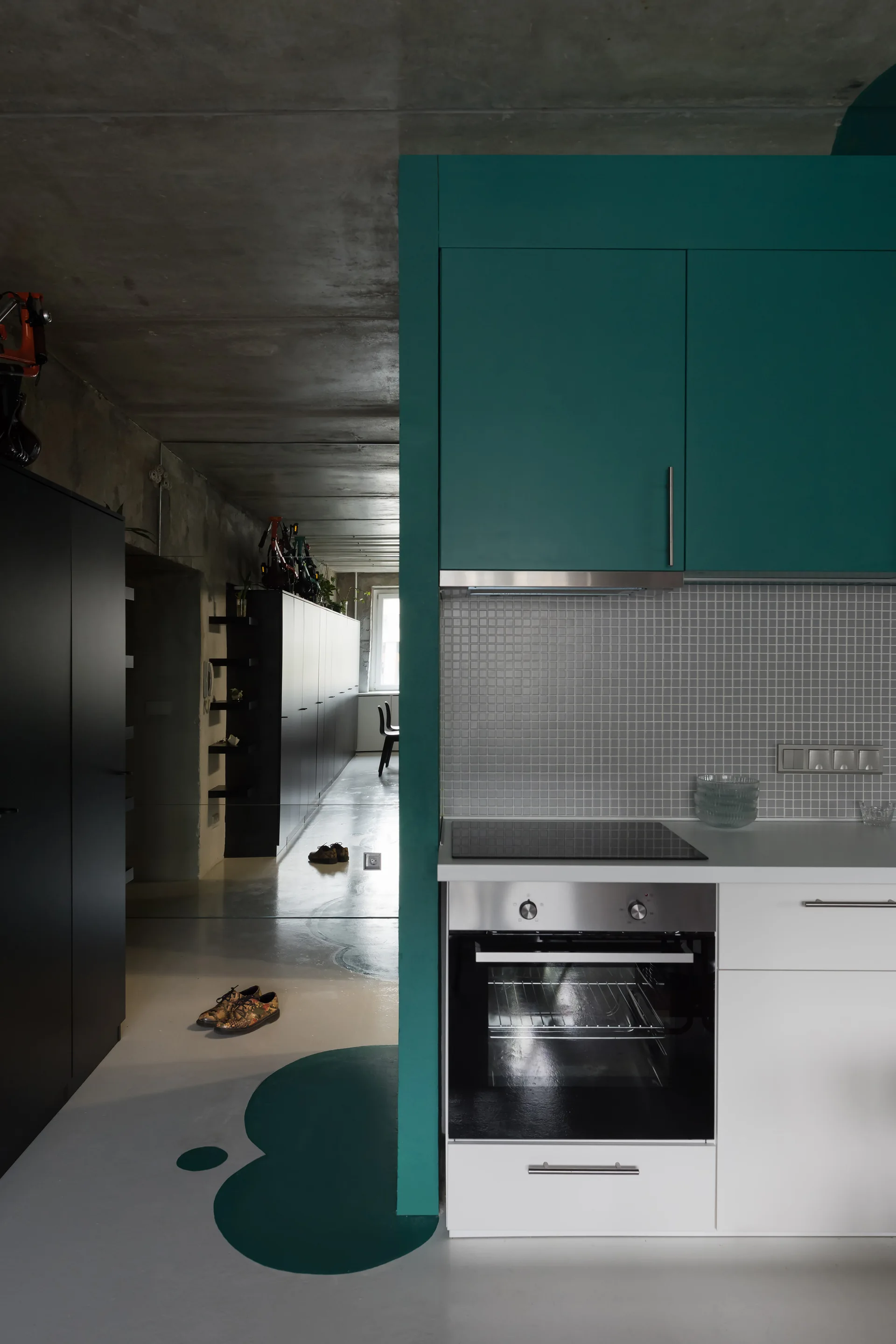 A modern kitchen features matte teal upper cabinets, white lower units, a small tile backsplash, and an exposed concrete ceiling.
